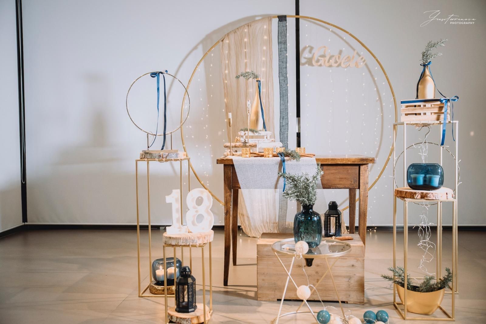 Elegante tavolo da dessert per matrimoni con cerchi dorati, fiori bianchi, candele e torta su uno sfondo bianco.