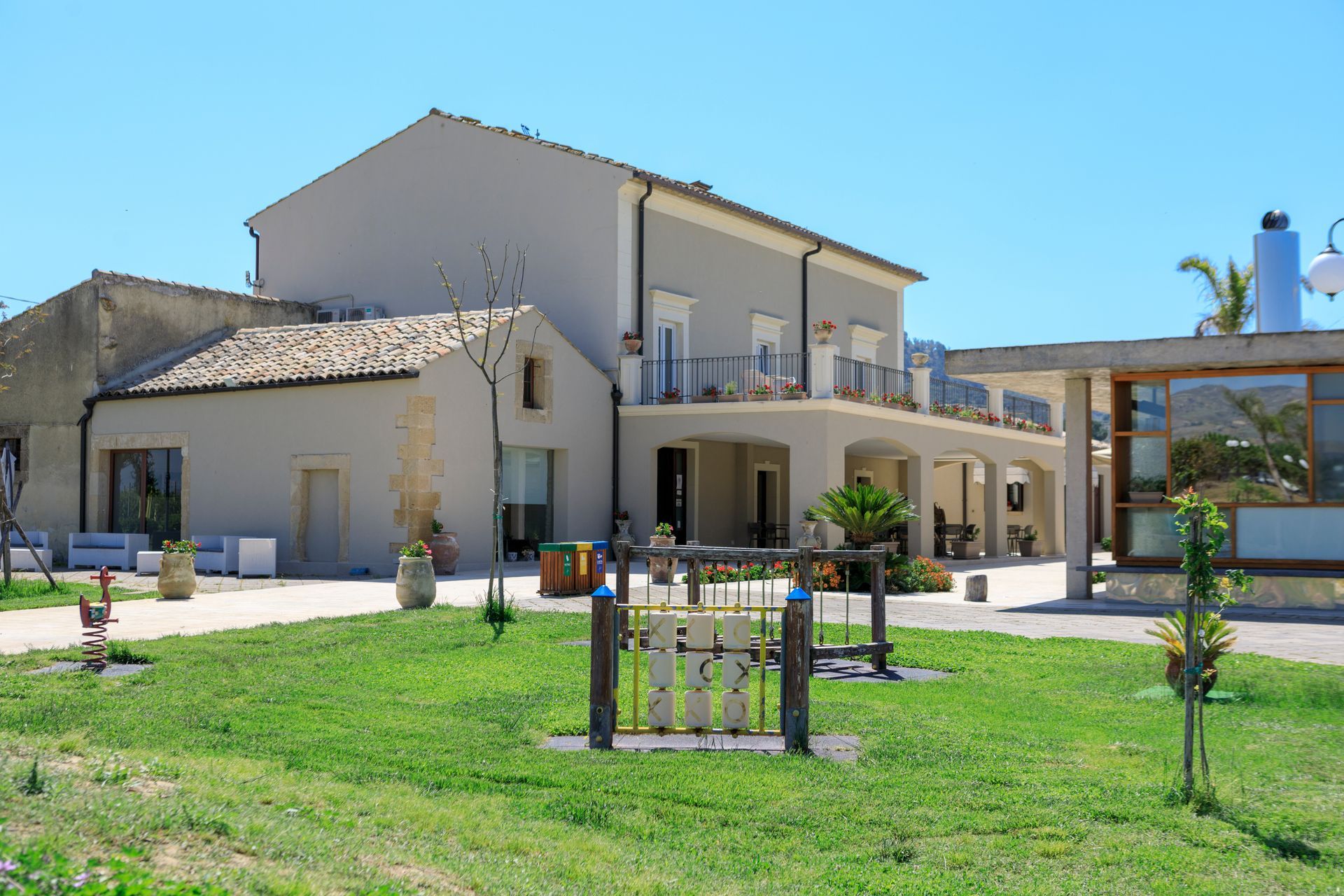 Casa moderna a due piani con balcone, patio e prato verde sotto un cielo azzurro limpido.