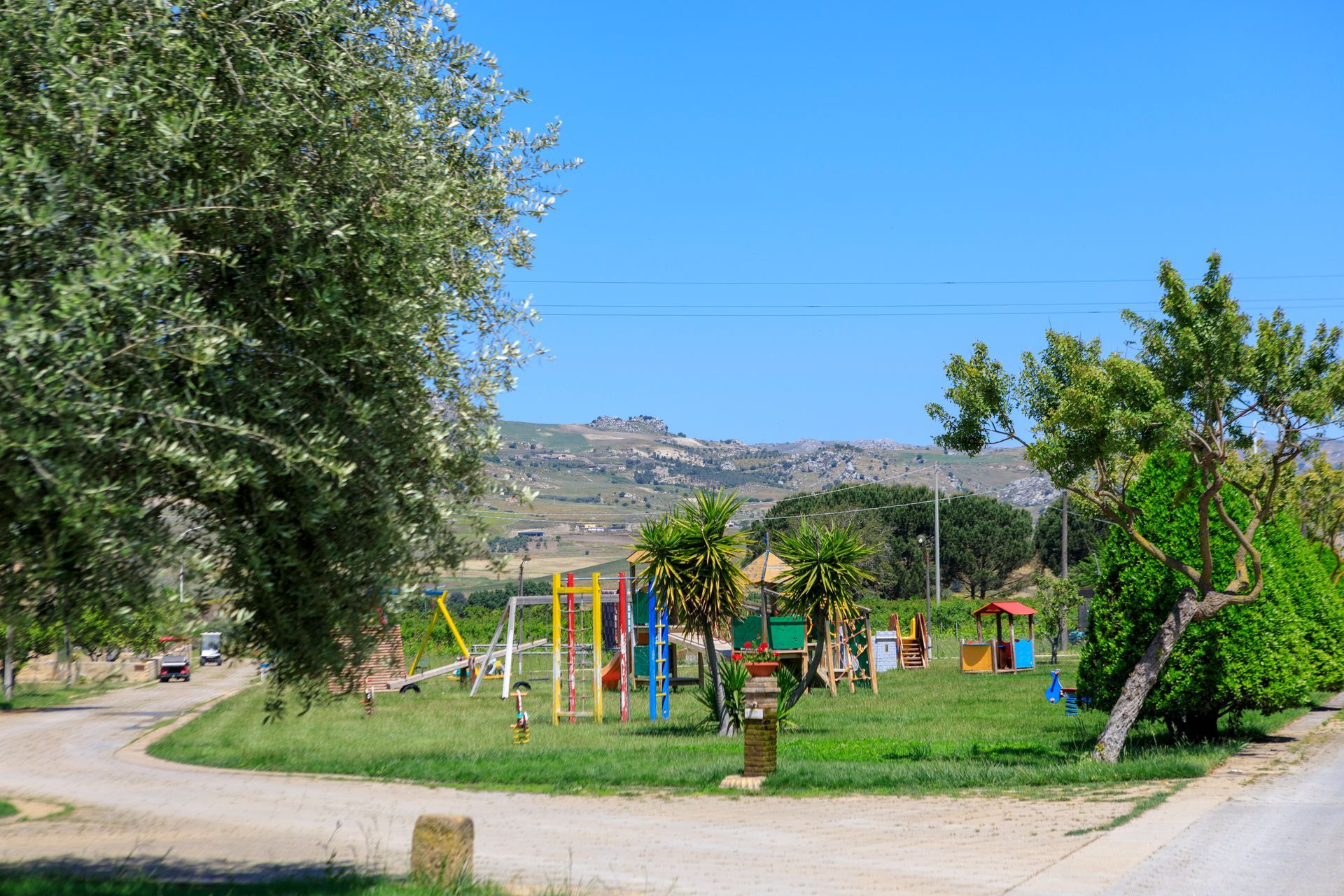 Piccolo parco giochi con attrezzature colorate, alberi verdi e colline sullo sfondo.