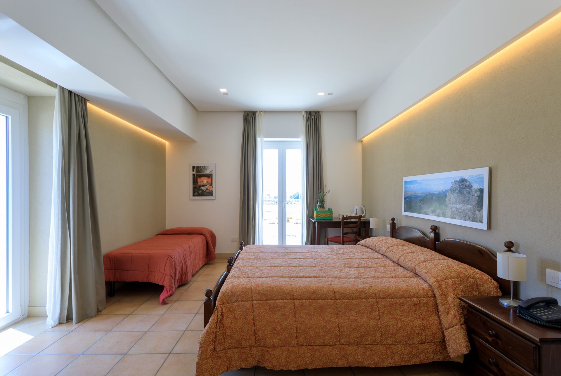 Luminosa camera d'albergo con due letti, luci calde, una finestra e una chaise longue rossa vicino alla parete.