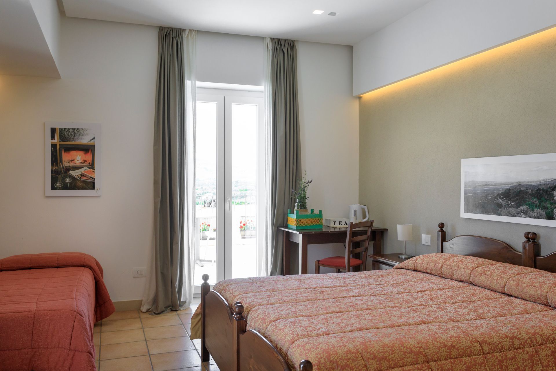 Luminosa camera d'albergo con due letti, una scrivania accanto alle porte finestre e una soffusa illuminazione a parete.