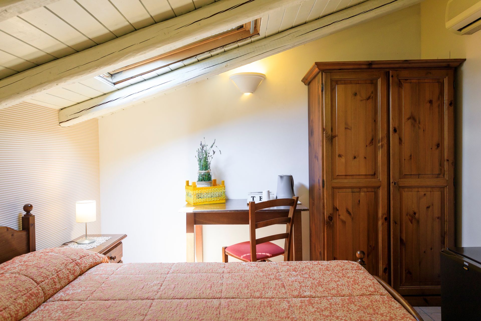 Camera da letto mansardata con due letti singoli, armadio in legno, scrivania e illuminazione.