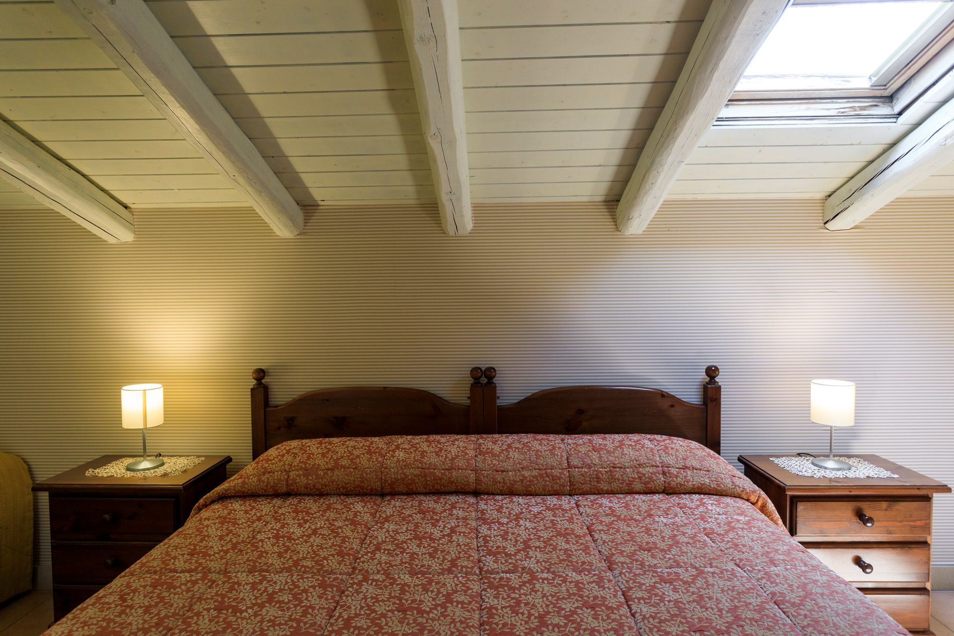 Camera da letto con letto in legno, due lampade da comodino e travi a vista bianche sul soffitto.