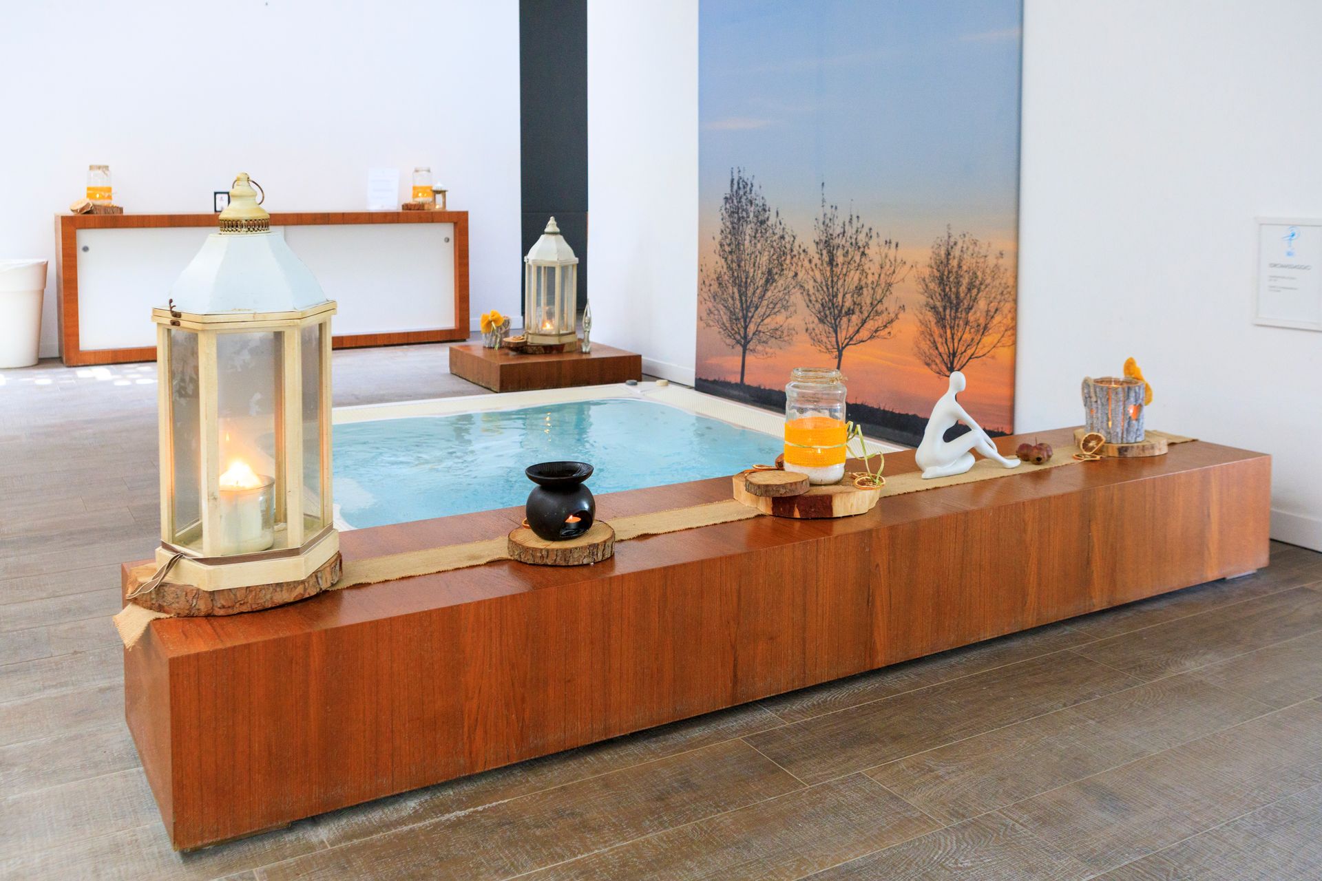 Esposizione in legno con lanterne illuminate, piccoli oggetti e un tavolo con piano blu in un luminoso spazio interno.