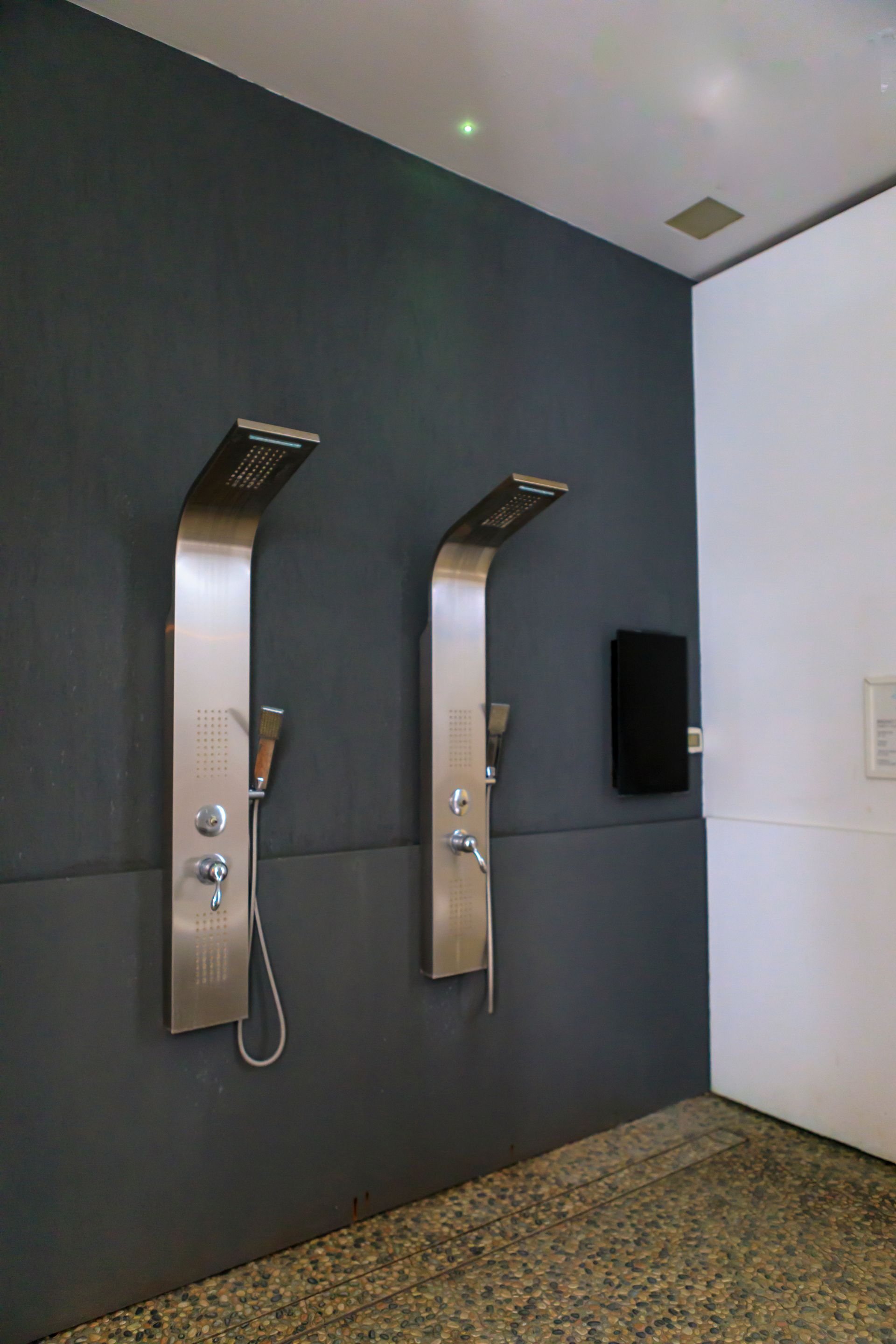 Due cabine telefoniche a muro in acciaio inossidabile in un corridoio con pareti grigio scuro e bianche.