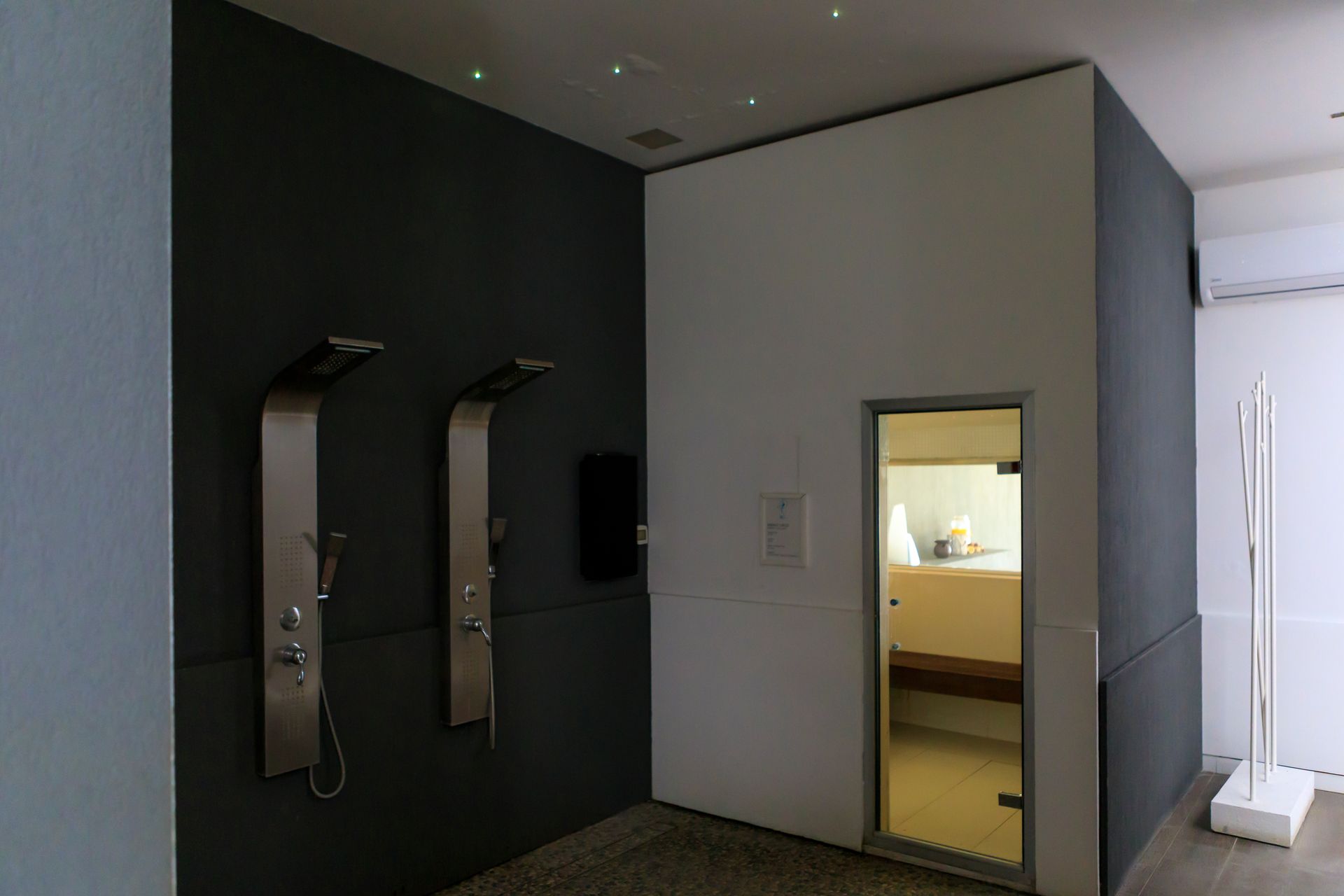 Corridoio moderno con telefoni scuri a parete, una porta e una stanza illuminata oltre.