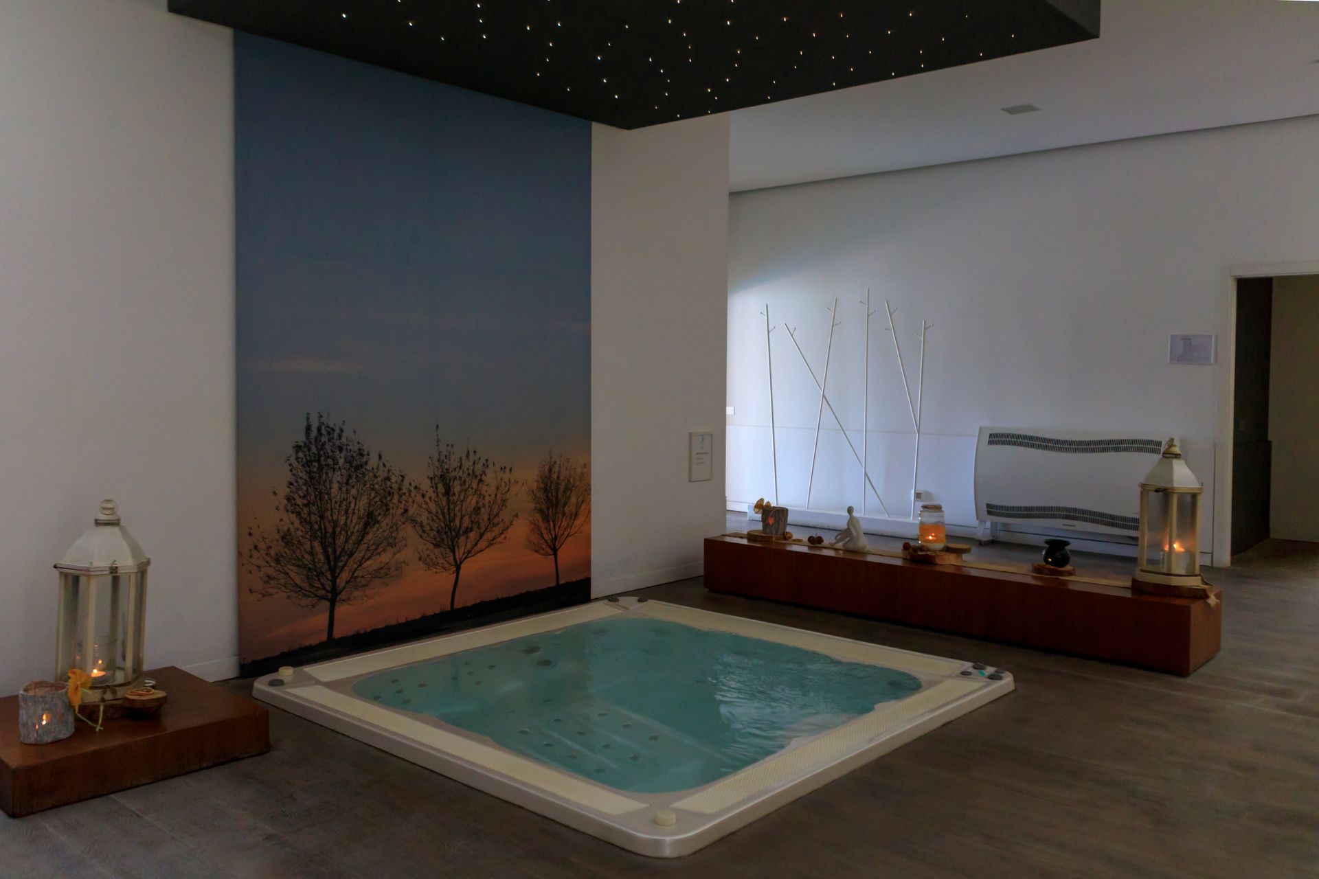 Sala benessere interna con piccola piscina quadrata, pavimento in legno, lanterne.
