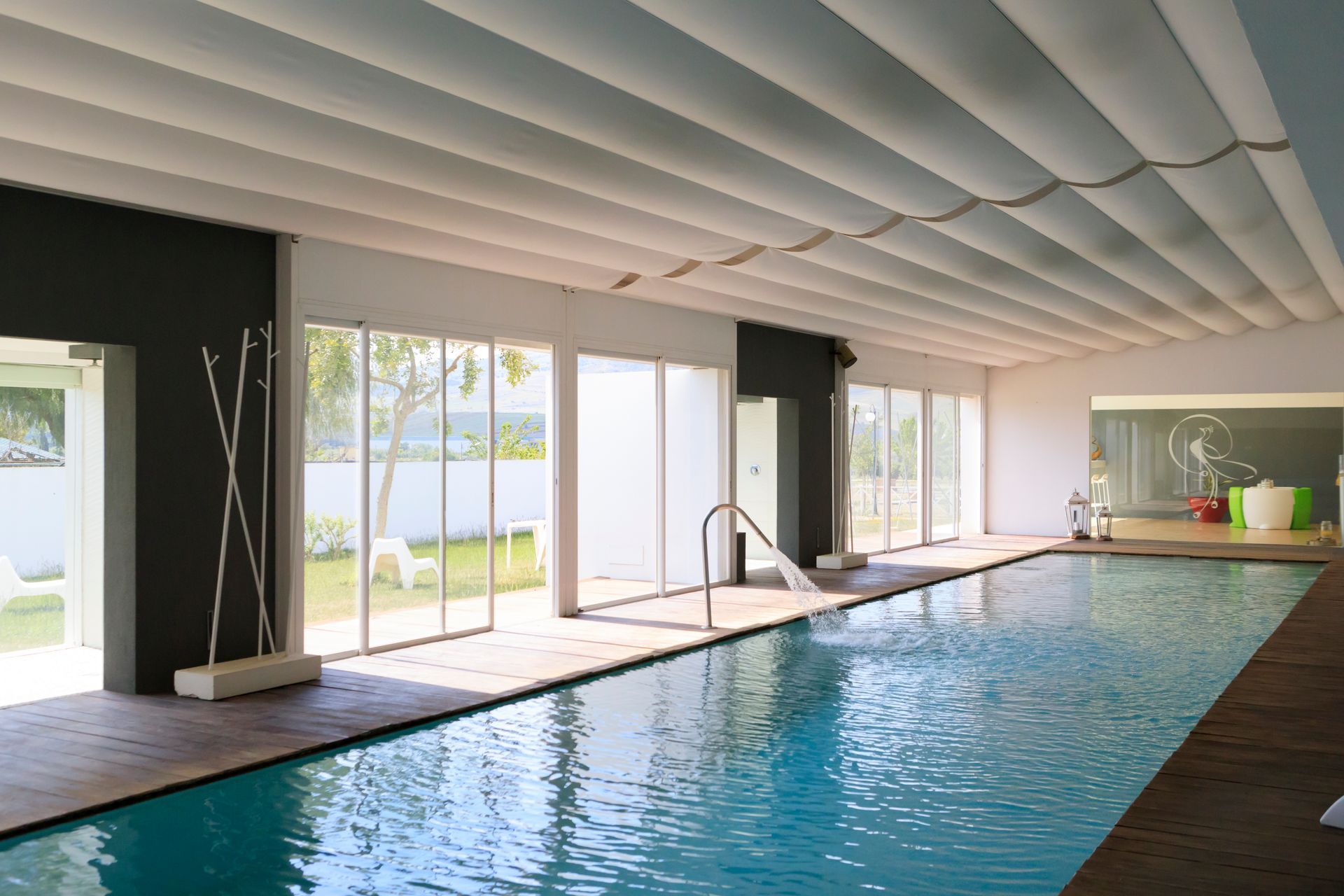 Piscina coperta per il nuoto, con ampie vetrate e terrazza in legno, in un ambiente moderno simile a una spa.