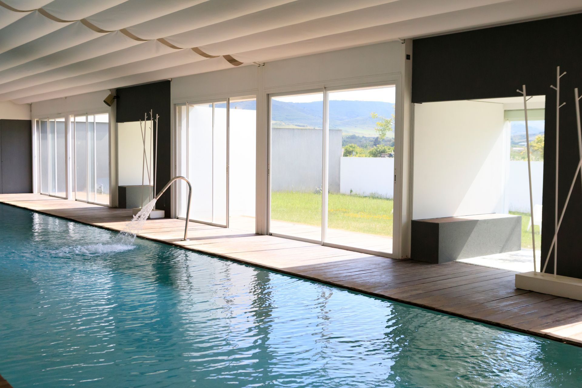 Piscina coperta con ampie finestre che si affacciano su un patio e un giardino erboso.