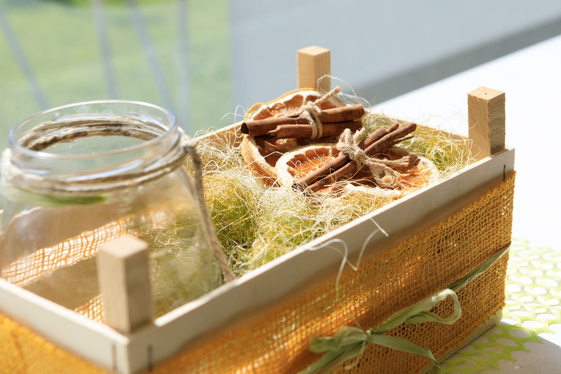 Vaso di vetro e vassoio di legno con erbe essiccate su muschio, illuminati dalla calda luce del sole