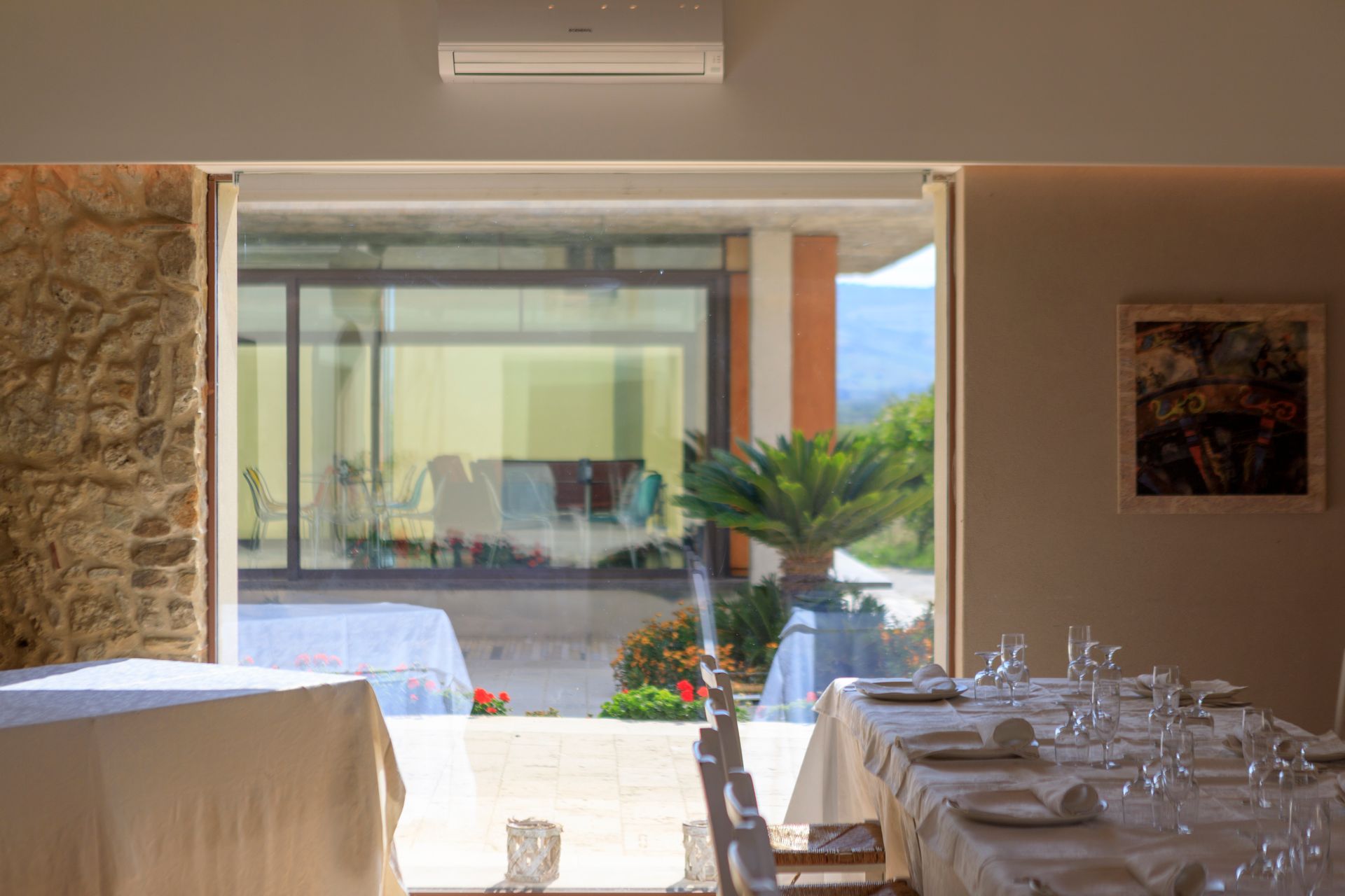 Elegante sala da pranzo con tavoli apparecchiati con colori bianchi, affacciata su un luminoso patio e sul giardino.