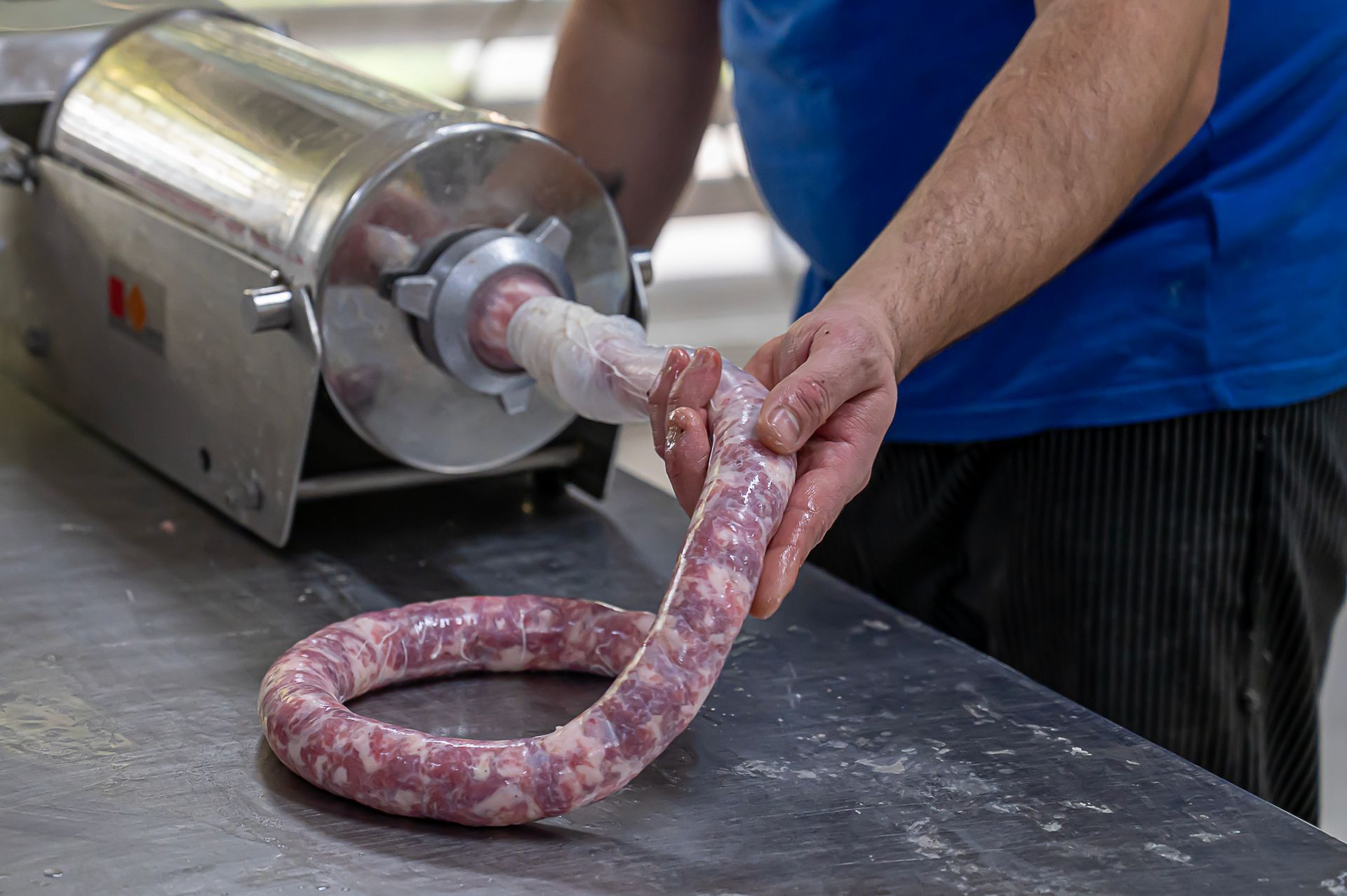 Una persona utilizza un insaccatrice per riempire una lunga salsiccia arrotolata su un bancone in acciaio inossidabile.