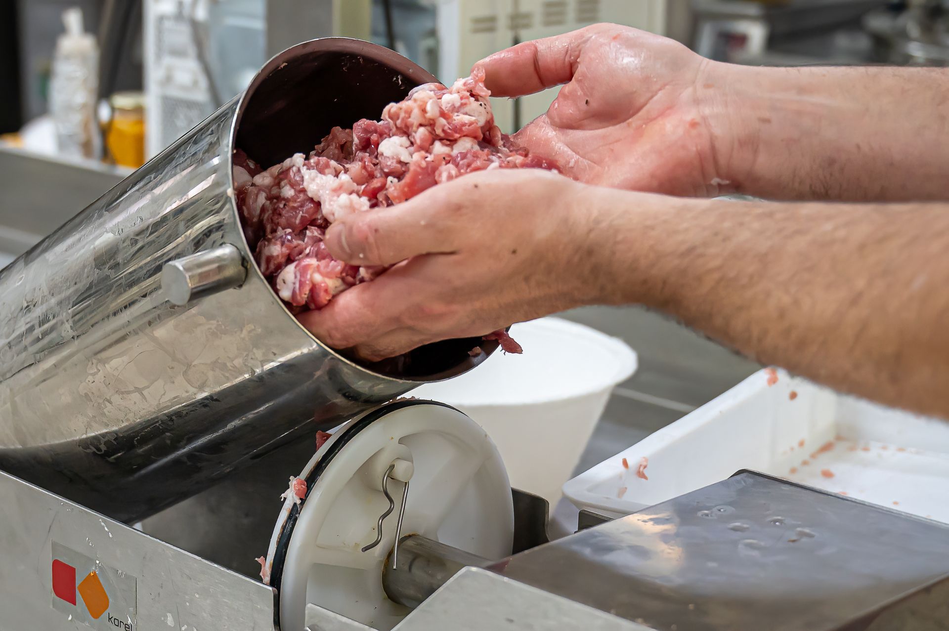 Mani che versano carne tritata in un tritacarne in acciaio inossidabile in una cucina.