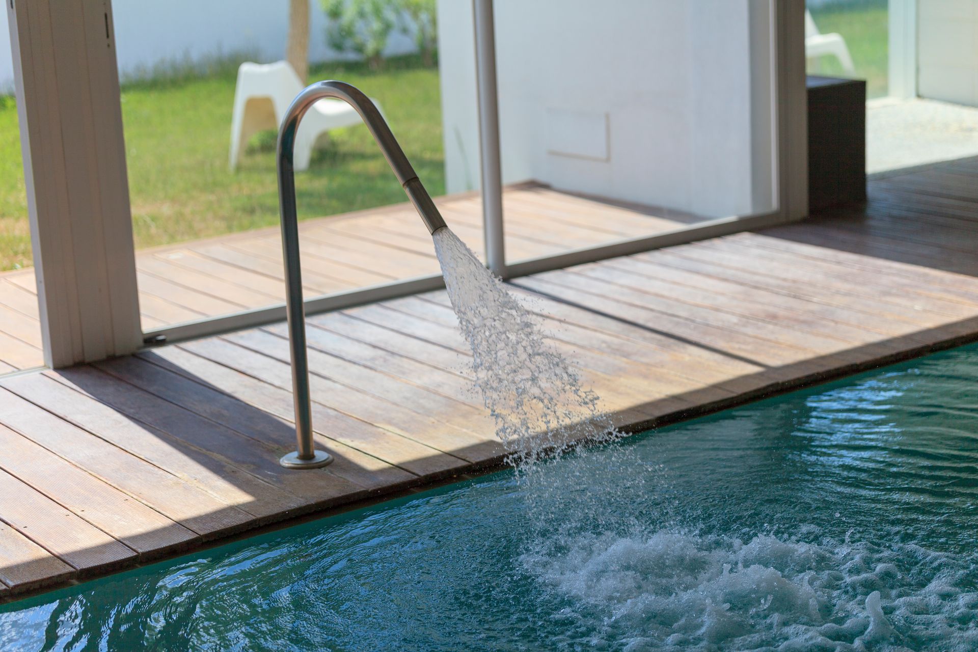 Bordo piscina coperto con fontana in acciaio inox che riversa acqua in una piscina blu.