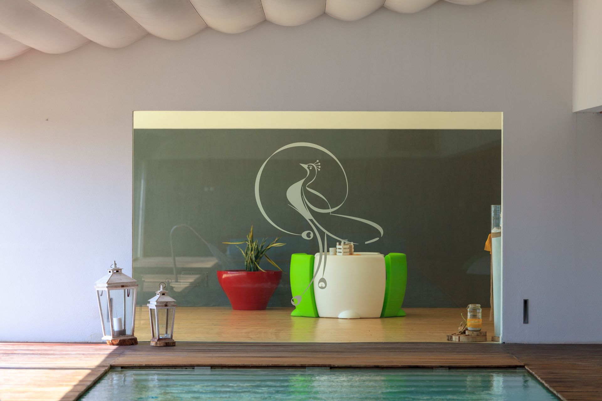 Moderna terrazza a bordo piscina con lavagna decorativa, piante in vaso, lanterne e piscina antistante.