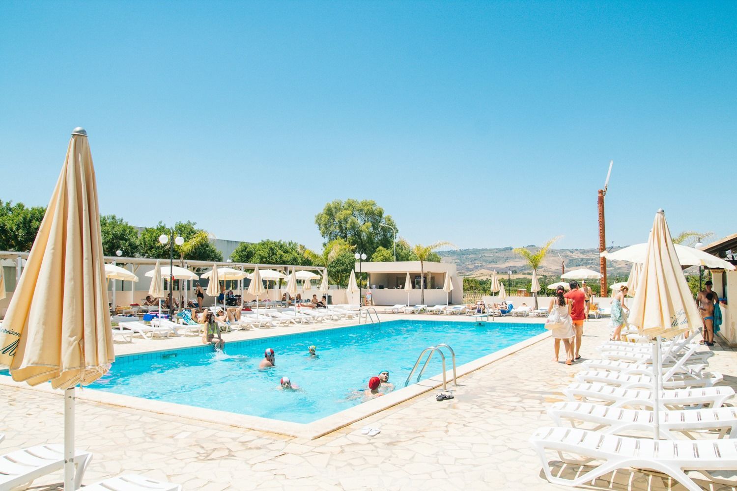 Piscina soleggiata del resort con lettini, ombrelloni e bagnanti