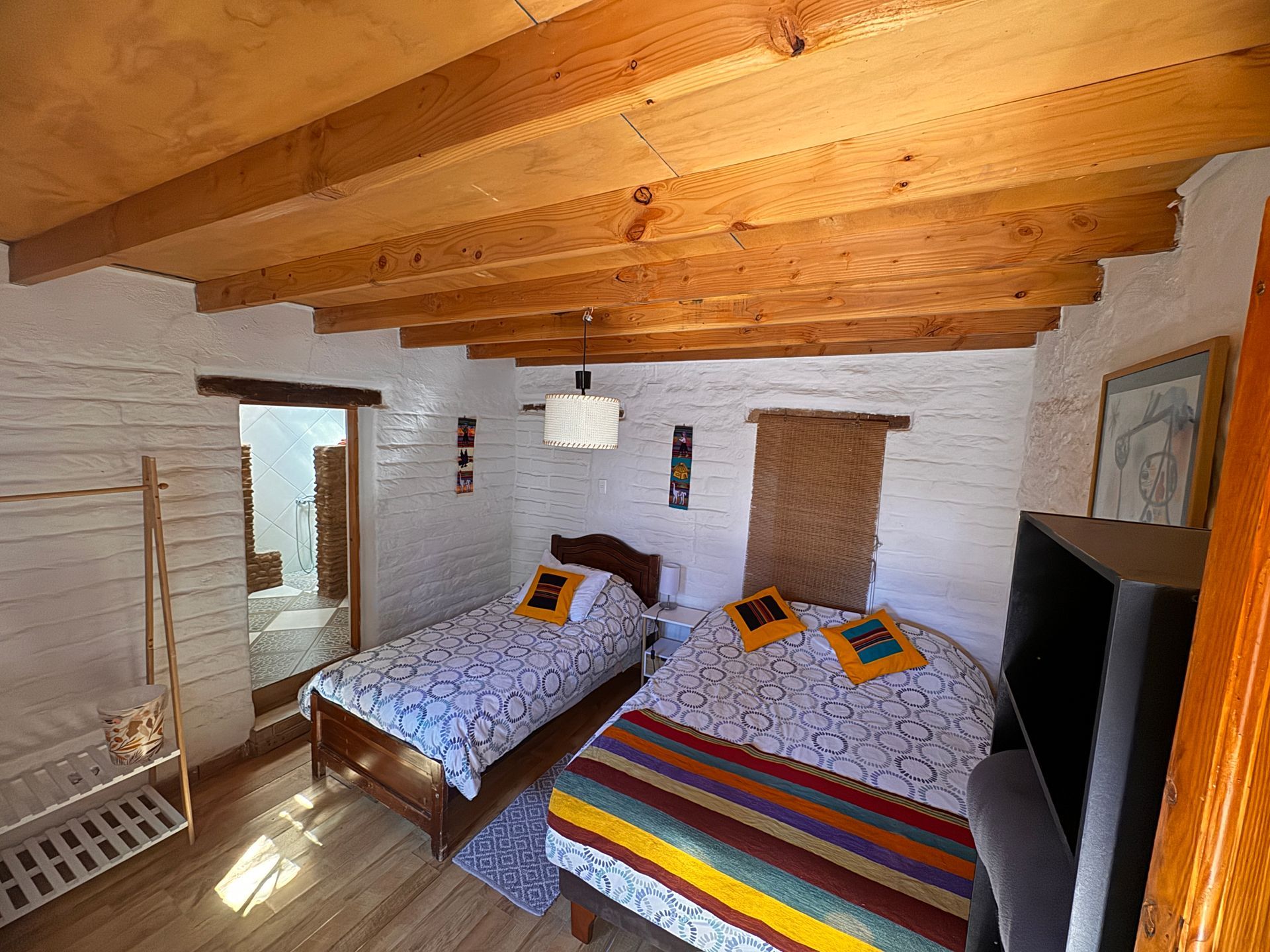 Habitación acogedora con dos camas individuales, paredes de ladrillo blanco y techo con vigas de madera.
