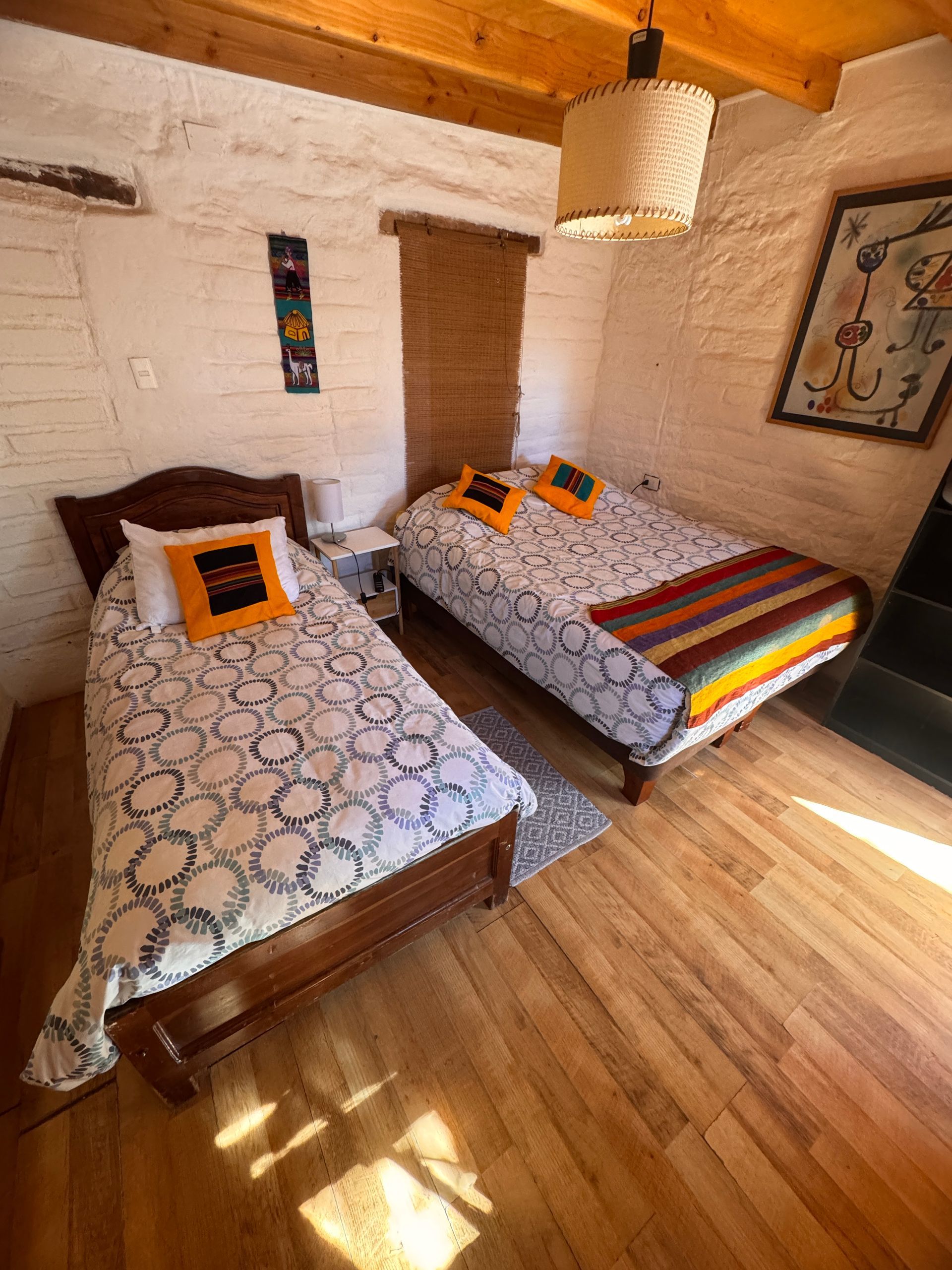 Acogedora habitación con dos camas individuales, colchas estampadas, suelo de madera y paredes de ladrillo blanco.