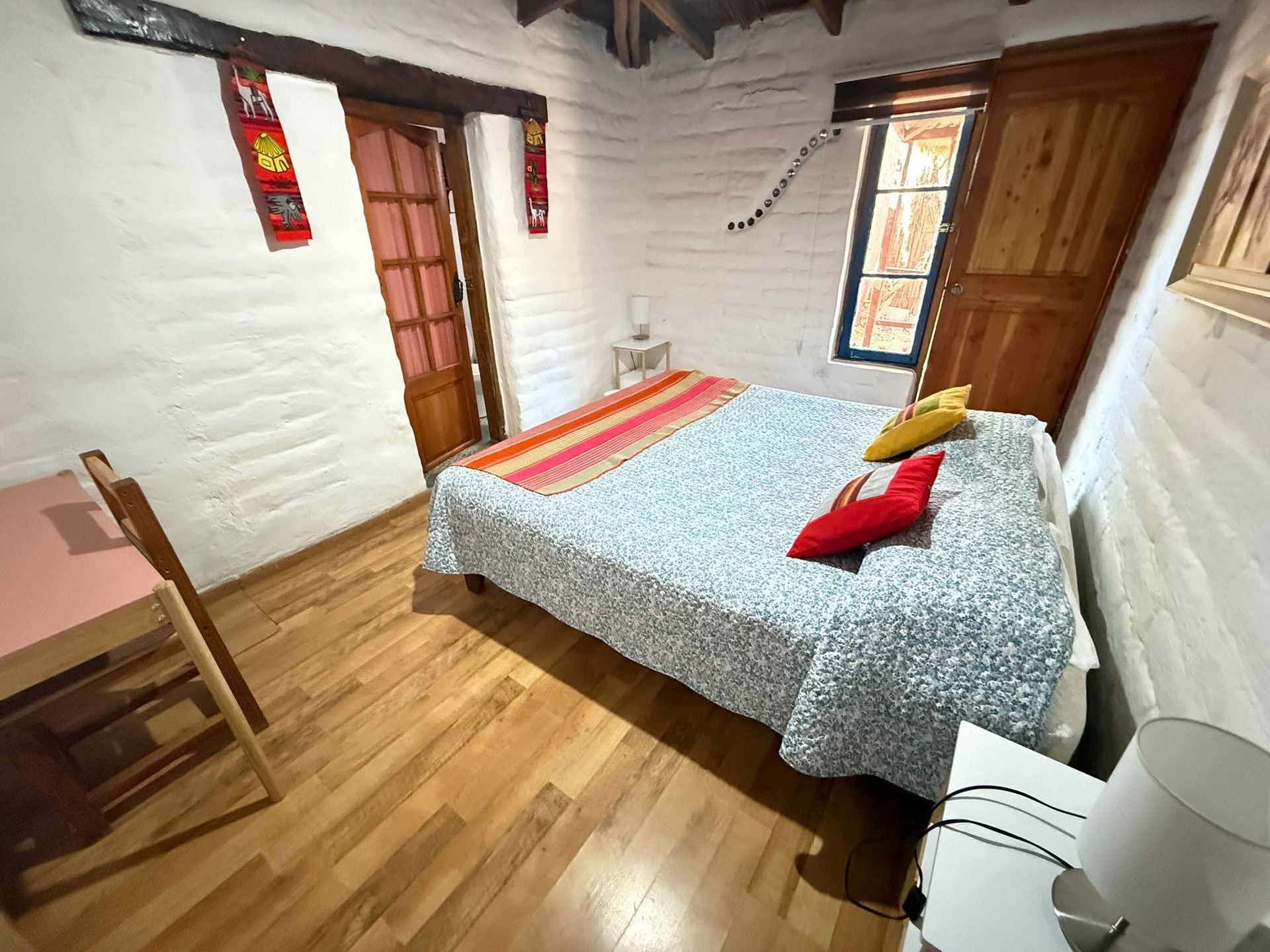Habitación luminosa con vigas de madera, una cama doble y paredes de ladrillo blanco.