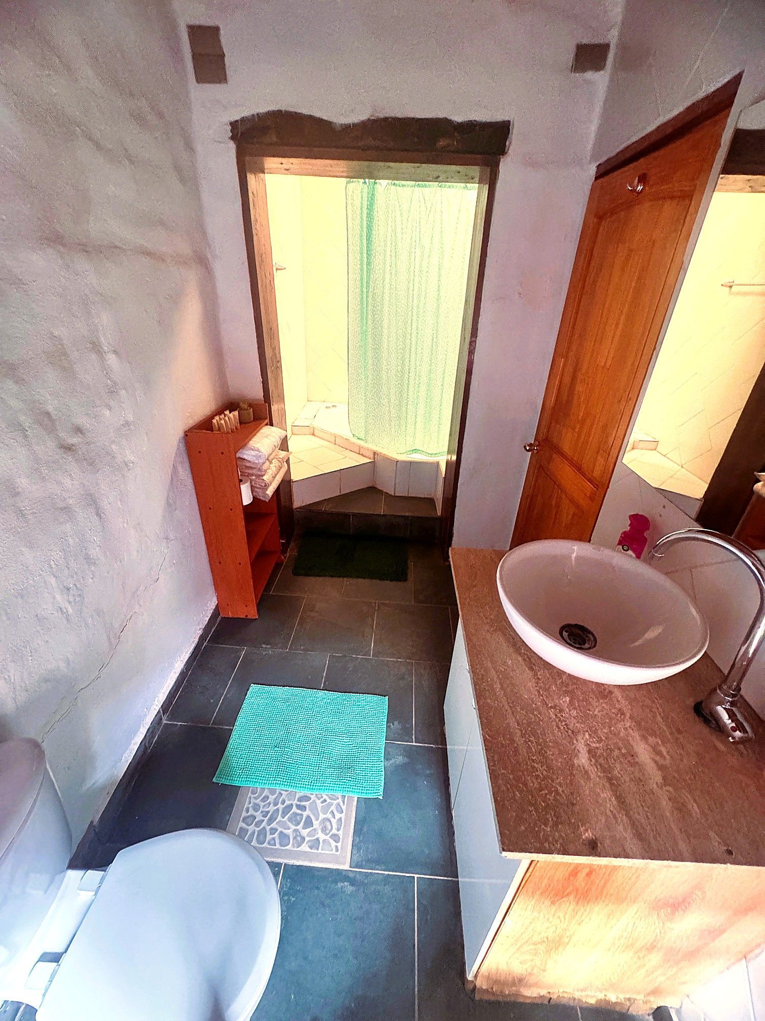 Baño estrecho con lavabo, inodoro, armario y suelo de baldosas, visto desde la puerta.