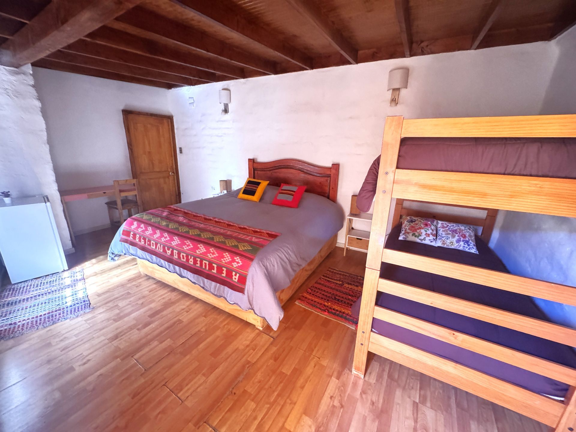 Dormitorio rústico con techo de madera, cama con edredón colorido y litera en una acogedora habitación estilo loft.