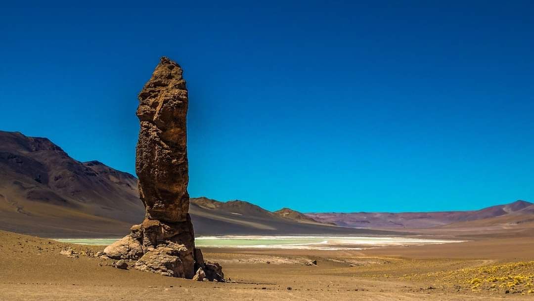 Alto pilar de roca en un paisaje desértico árido bajo un cielo azul claro.