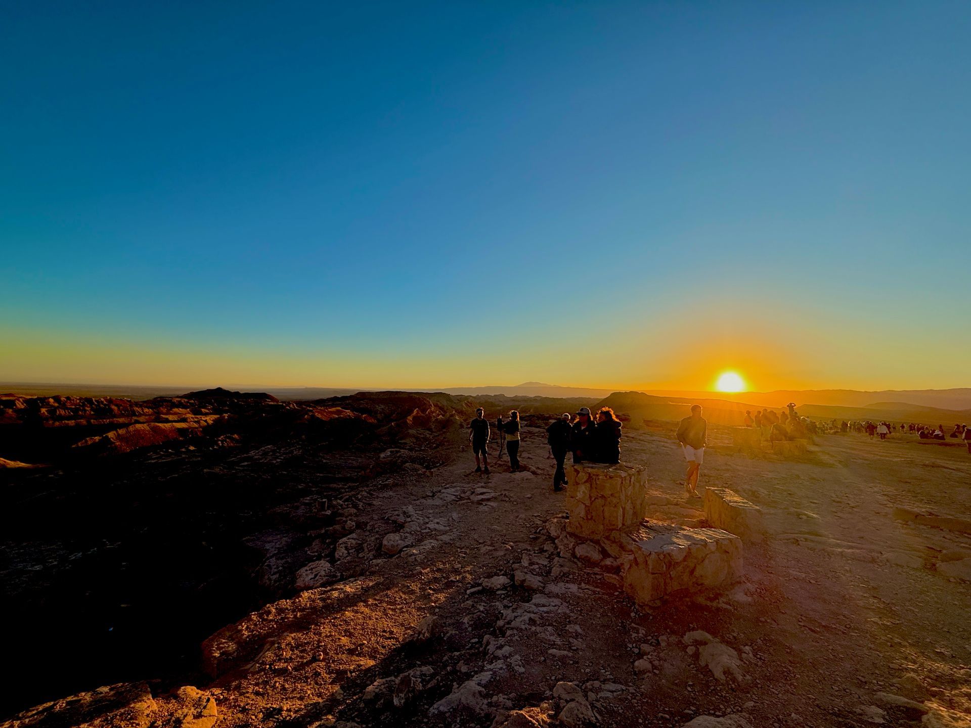Puesta de sol sobre un sendero rocoso con algunos excursionistas recortados contra el cielo azul.