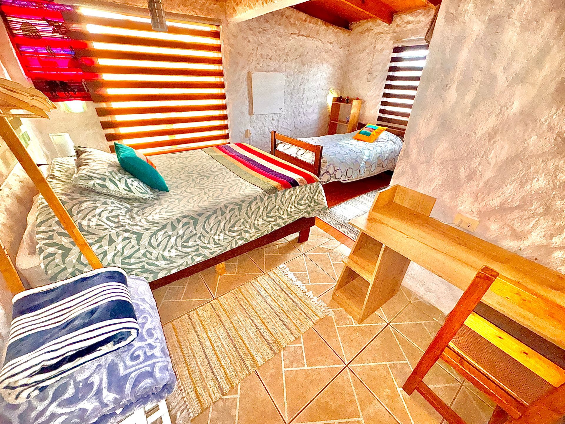 Acogedora habitación rústica con dos camas, cortinas a rayas, paredes de madera y suelo de baldosas.