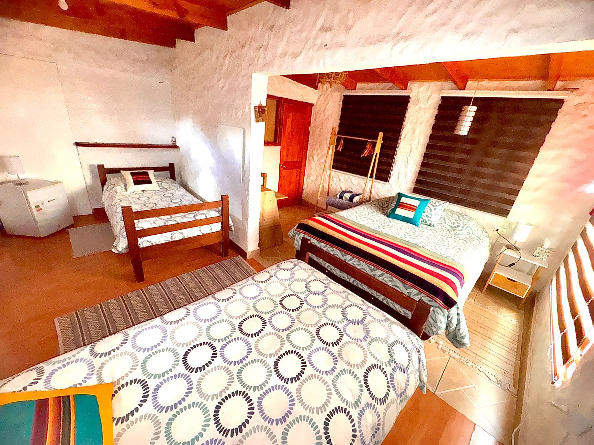 Habitación acogedora con dos camas, paredes blancas, vigas de madera y ropa de cama estampada.