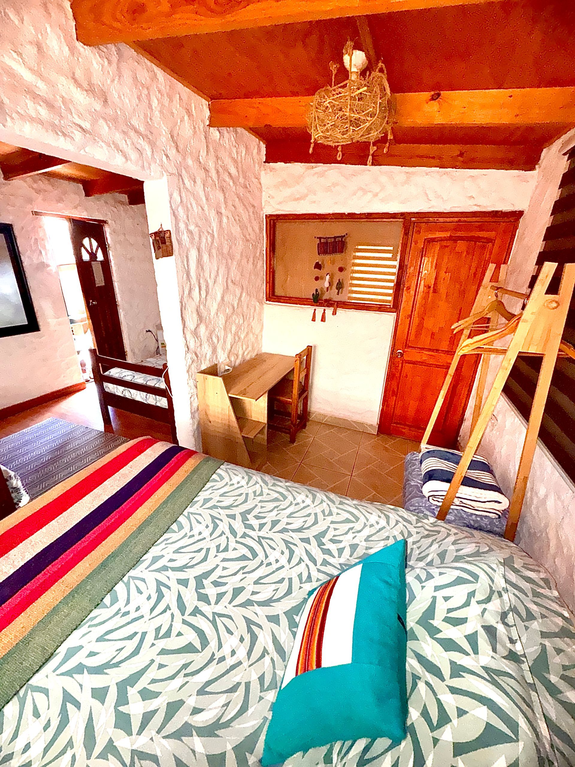 Acogedora habitación con alfombra a rayas, cama, escritorio, escalera, vigas de madera y paredes de color naranja cálido.