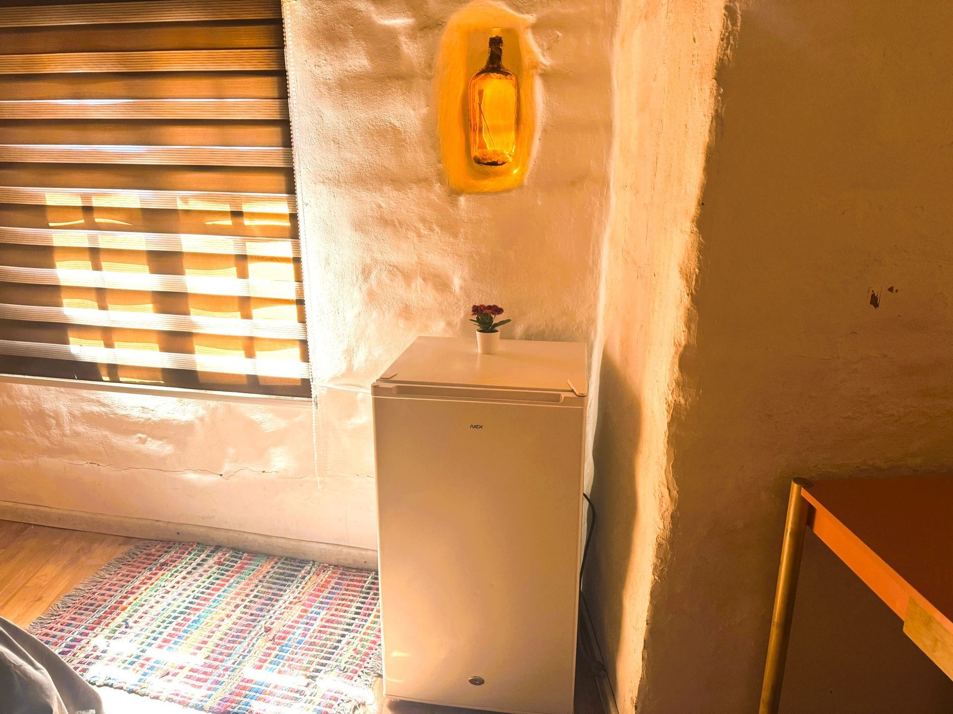 Baño pequeño con lavabo blanco, espejo de pared, persianas y una alfombra colorida.