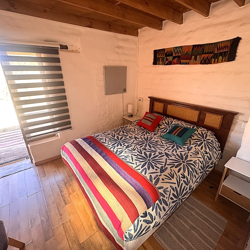 Un dormitorio acogedor con una colcha estampada, una manta a rayas, un cabecero de madera y vigas de techo a la vista.