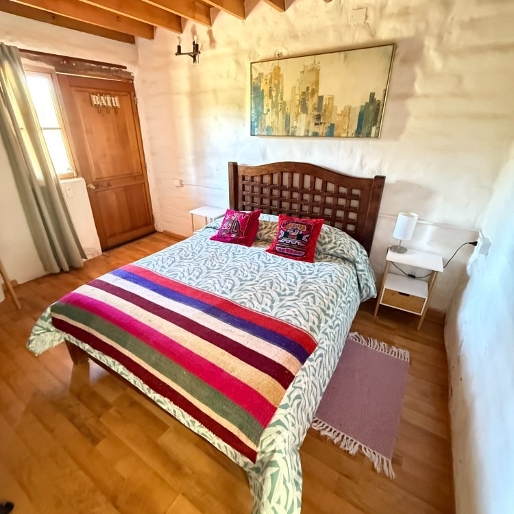 Habitación acogedora con cama de madera, manta de rayas coloridas, paredes blancas y suelo de madera.