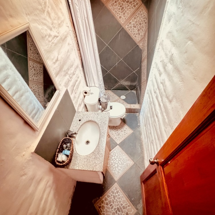 Vista desde un ángulo elevado de un baño compacto con lavabo blanco, inodoro y una zona de ducha alicatada tras una cortina.