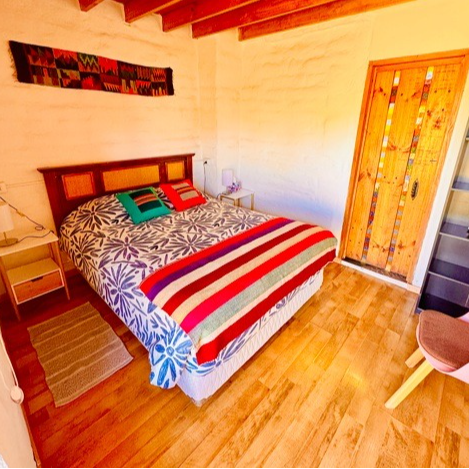Habitación acogedora con cama, manta a rayas, suelo de madera y puerta de color naranja brillante.