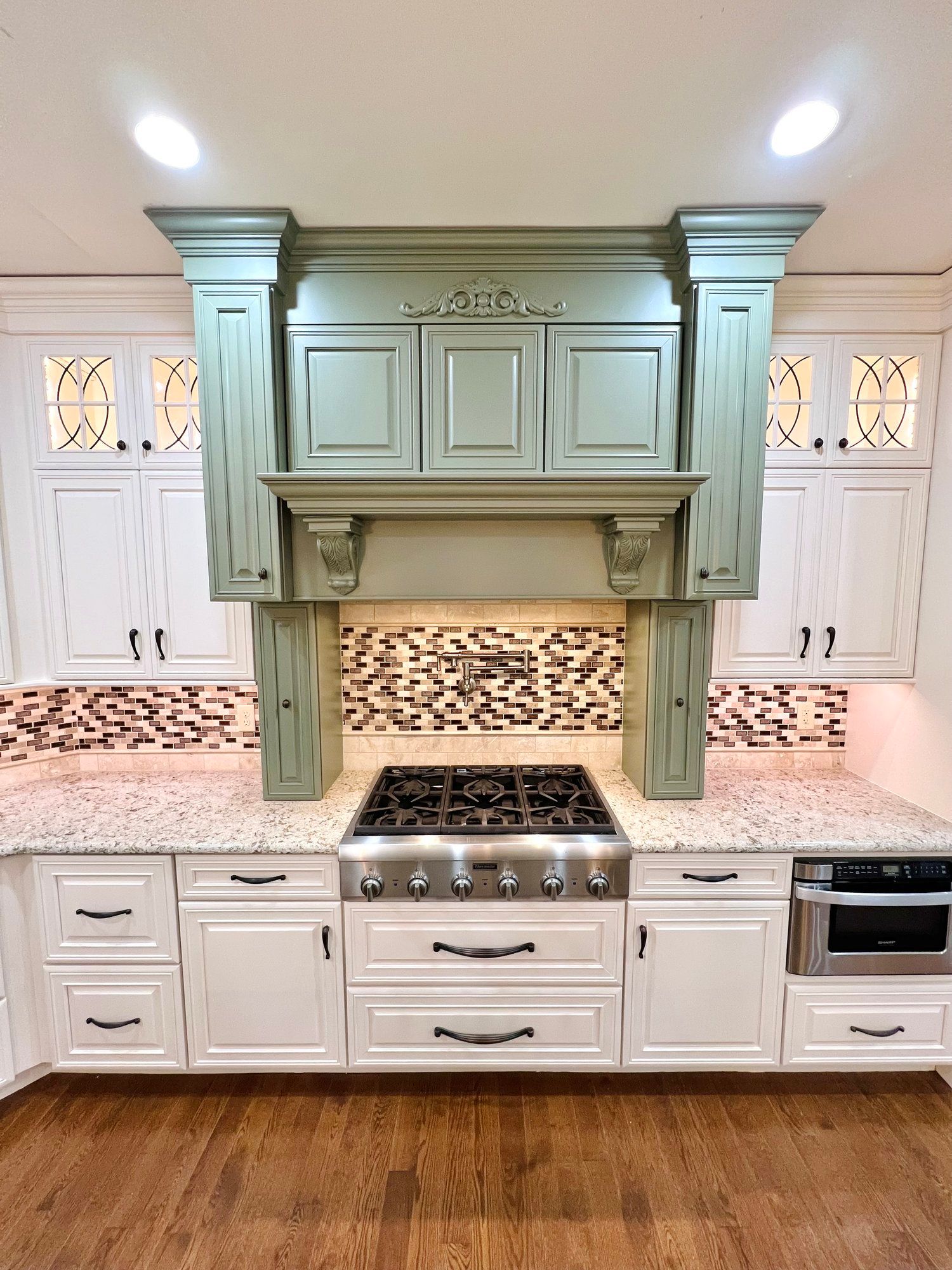 Kitchen with white cabinets, granite countertops, and a sage green range hood.