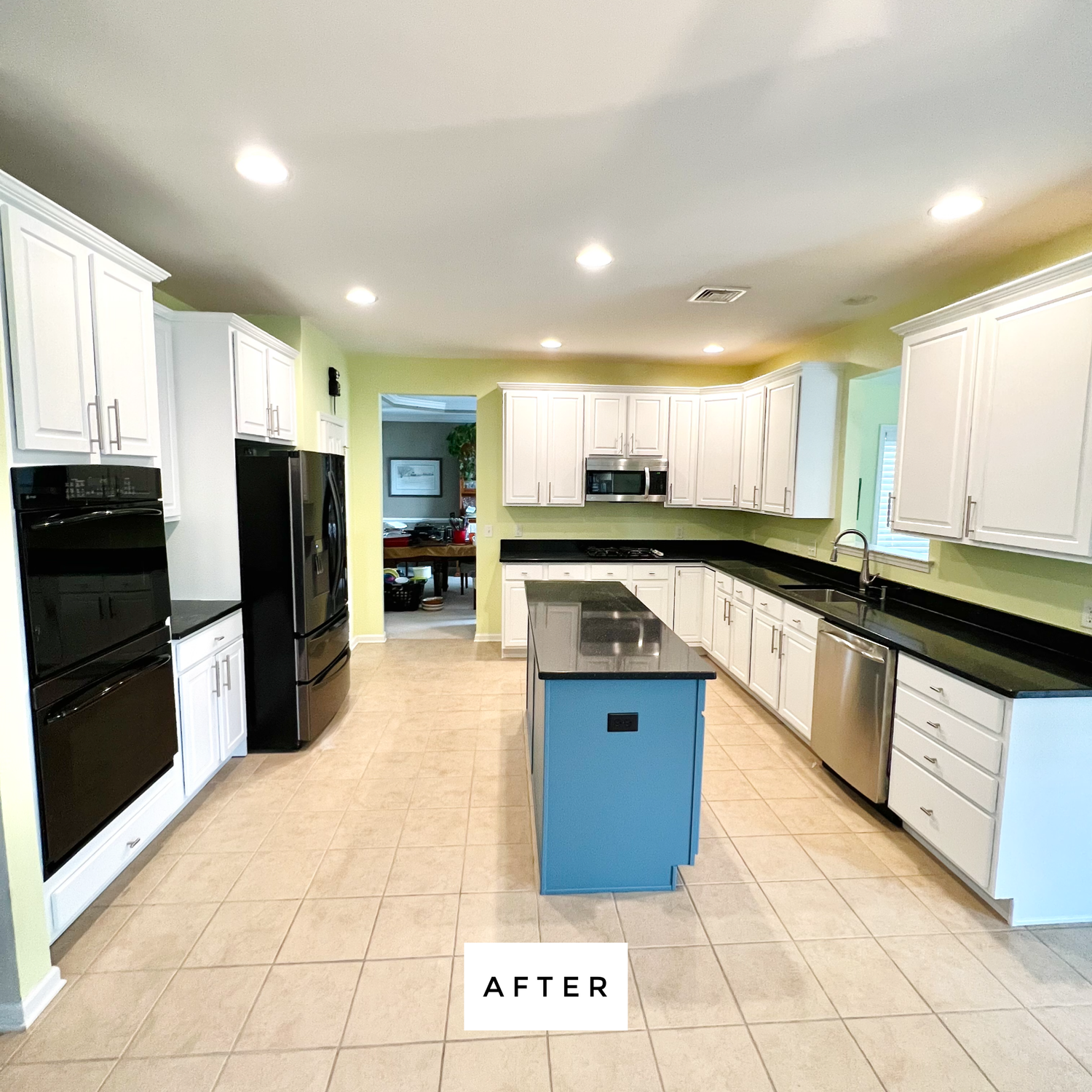 Newly renovated kitchen with white cabinets, black appliances, blue island, and beige tile floor.