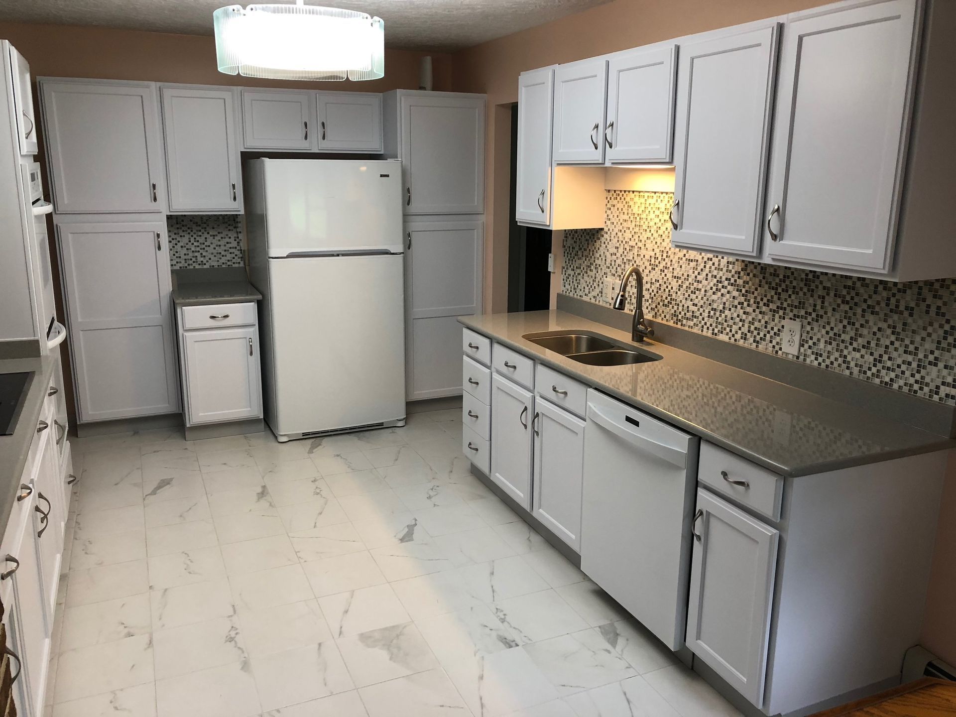 Kitchen with white cabinets, appliances, and countertops; tiled backsplash, light flooring.