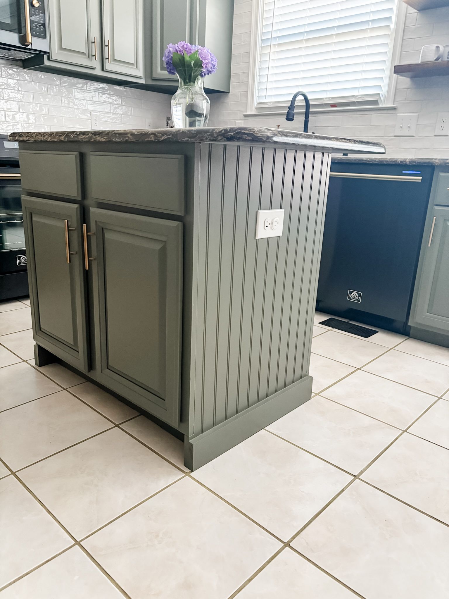 Kitchen island painted olive green with a patterned side, cabinets, and a granite countertop.