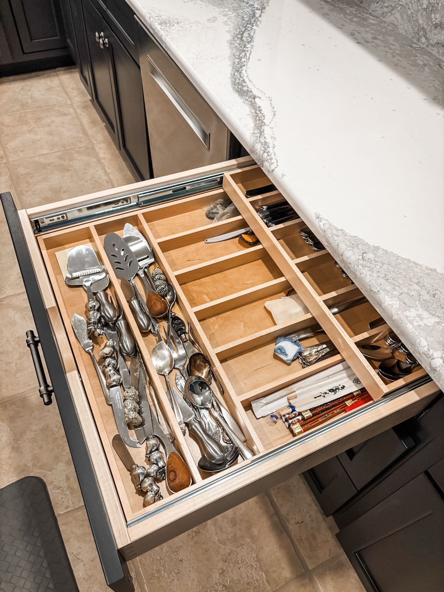 Open kitchen drawer with custom wooden dividers holding silverware and cooking utensils.