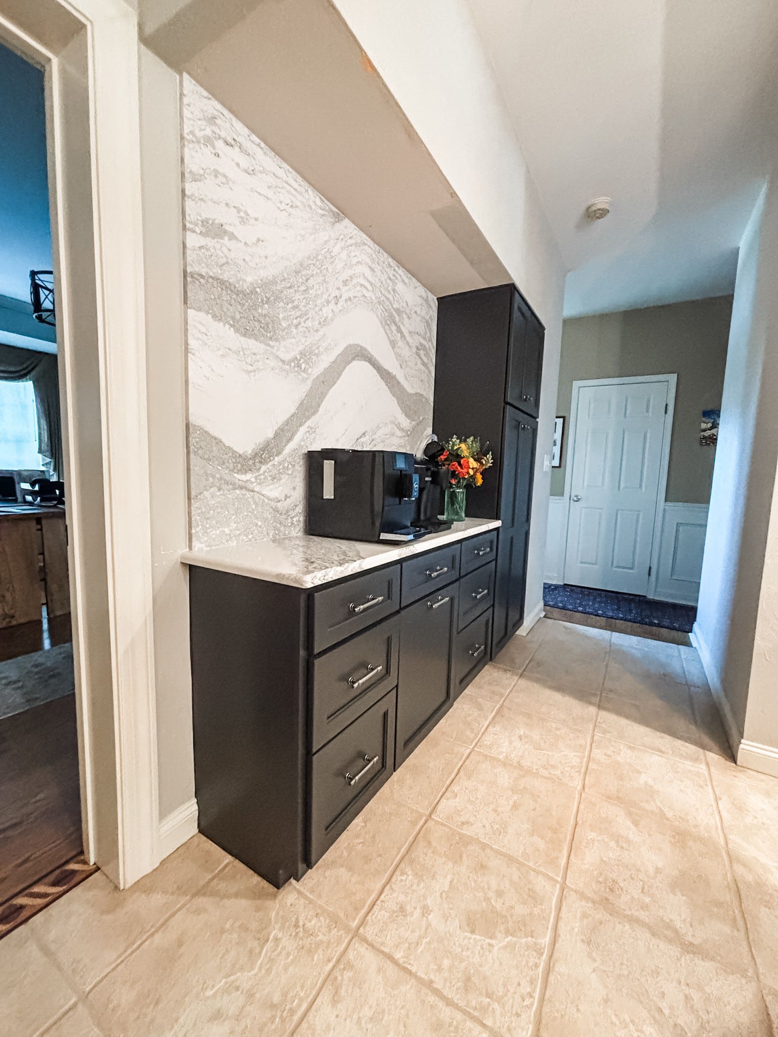 Dark gray cabinetry with coffee machine, backsplash, and hallway.