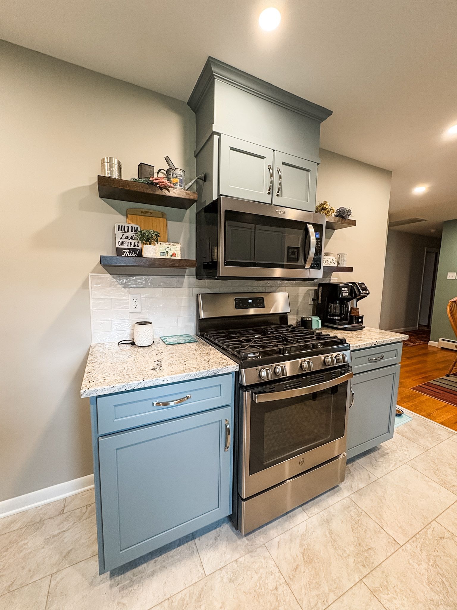 Blue kitchen with stainless steel appliances, shelves with decor.