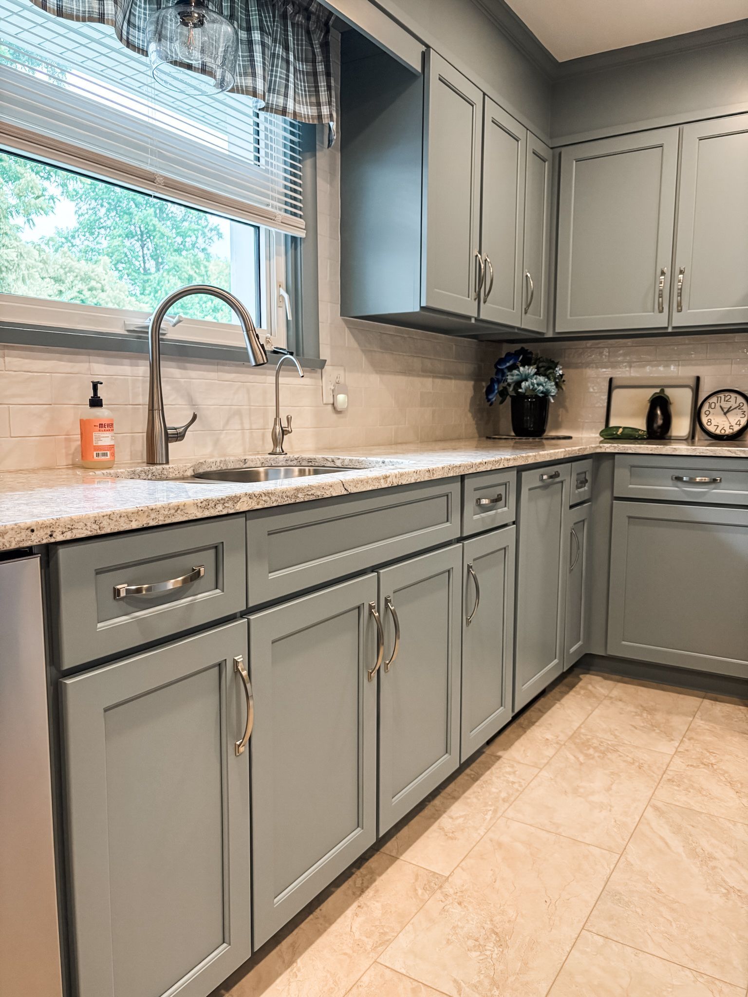 Kitchen with gray cabinets, granite countertops, and light-colored tile backsplash and flooring.