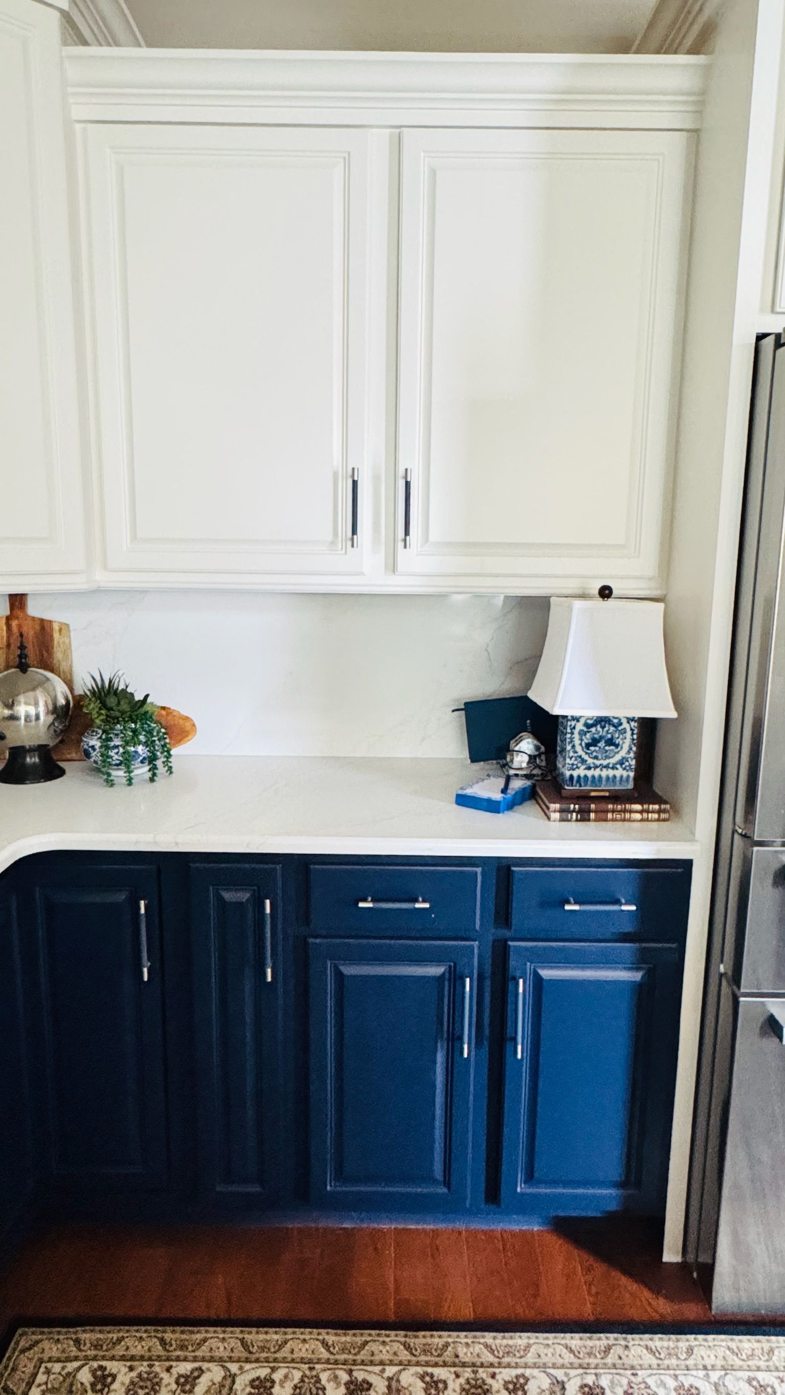 Two-tone kitchen cabinets; white uppers, navy lowers, white countertop, lamp, and decor.