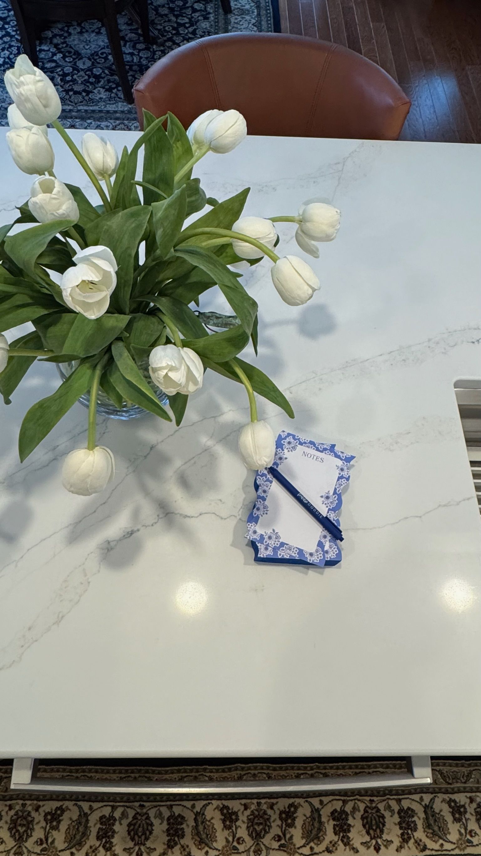 White tulips in a vase on a white countertop, notepad and pen.