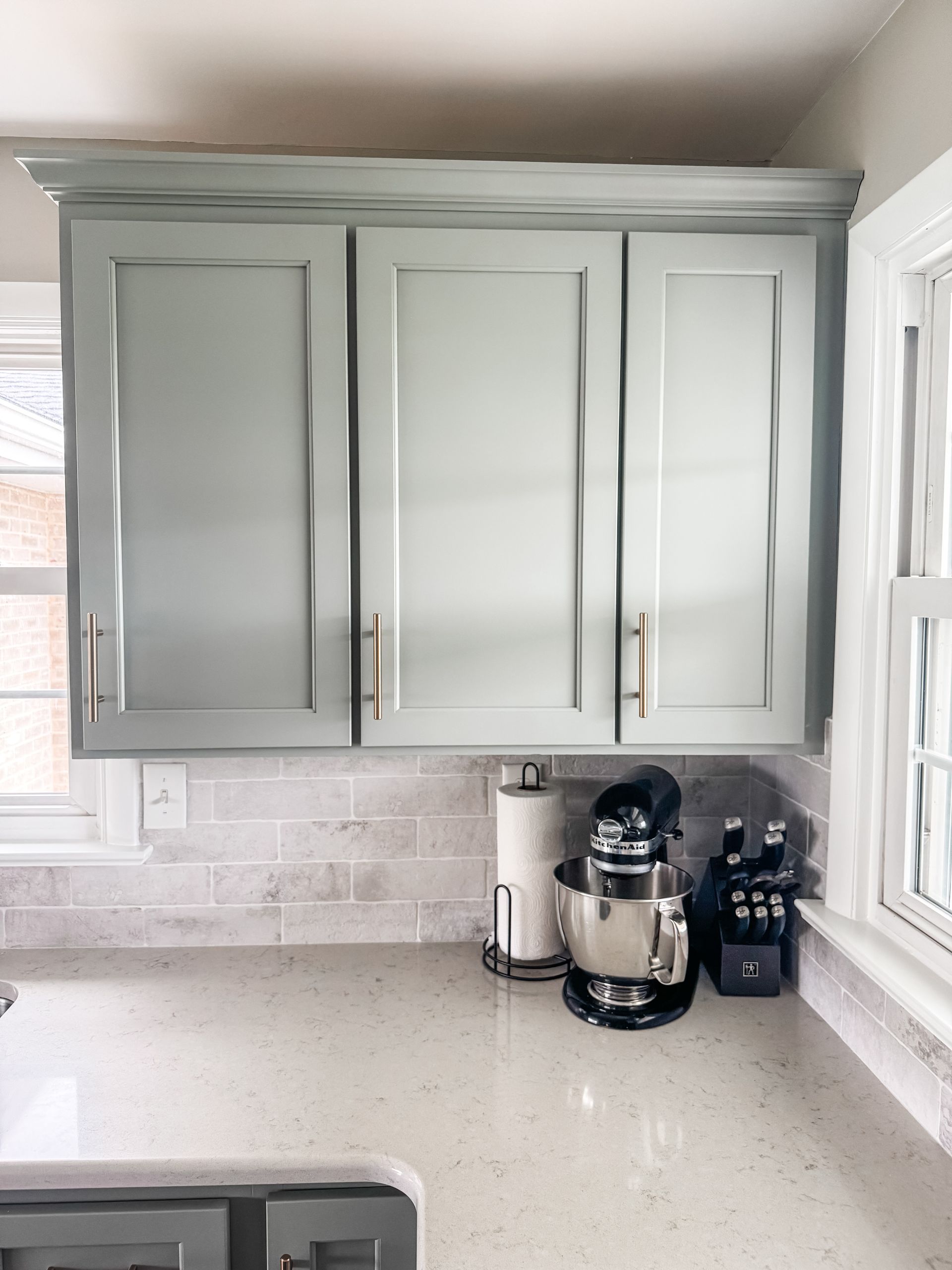 Light blue kitchen cabinets above a countertop with a mixer and knife block.
