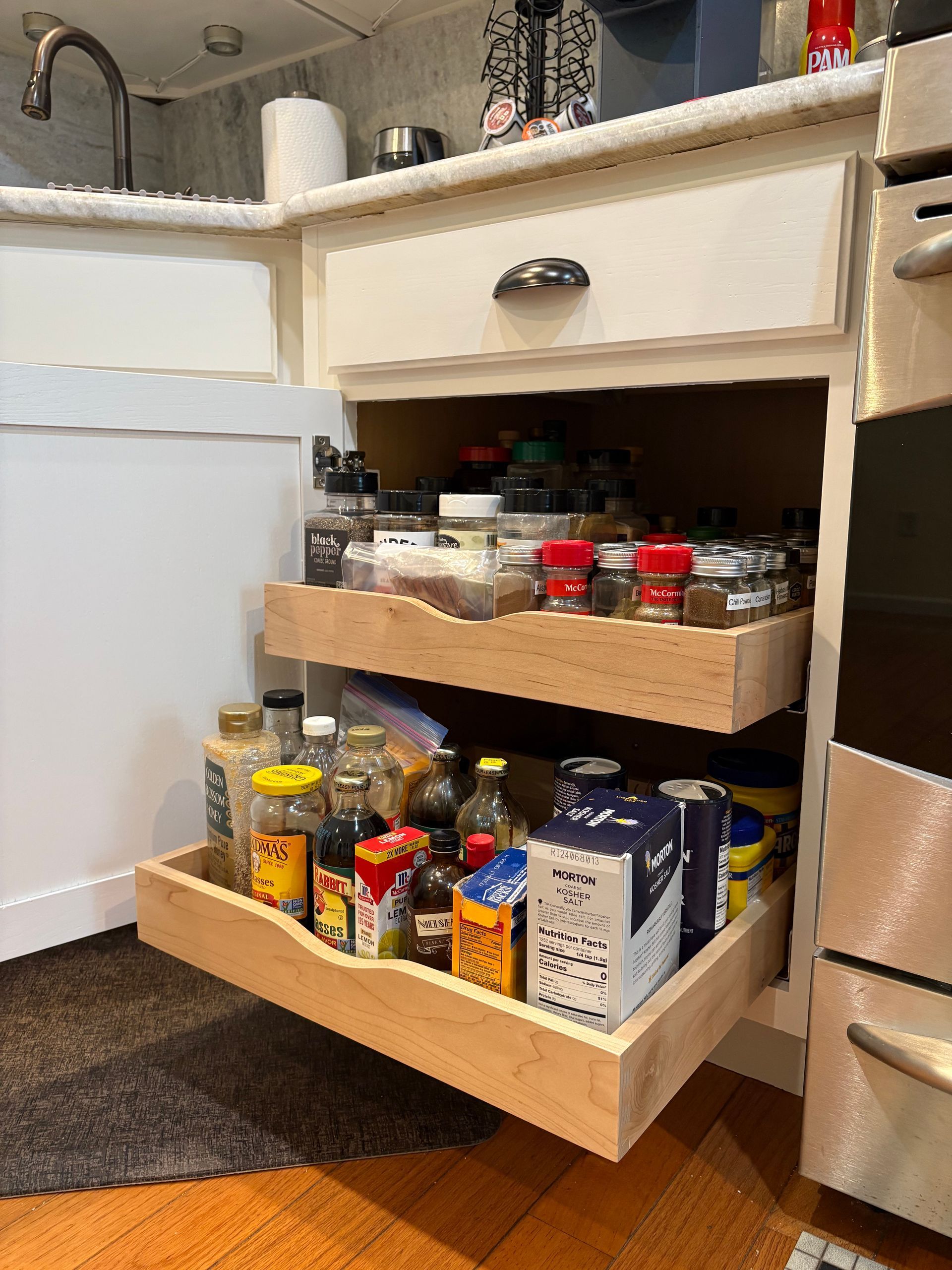 Two wooden pull-out shelves inside a white kitchen cabinet, holding white ceramic dishes.
