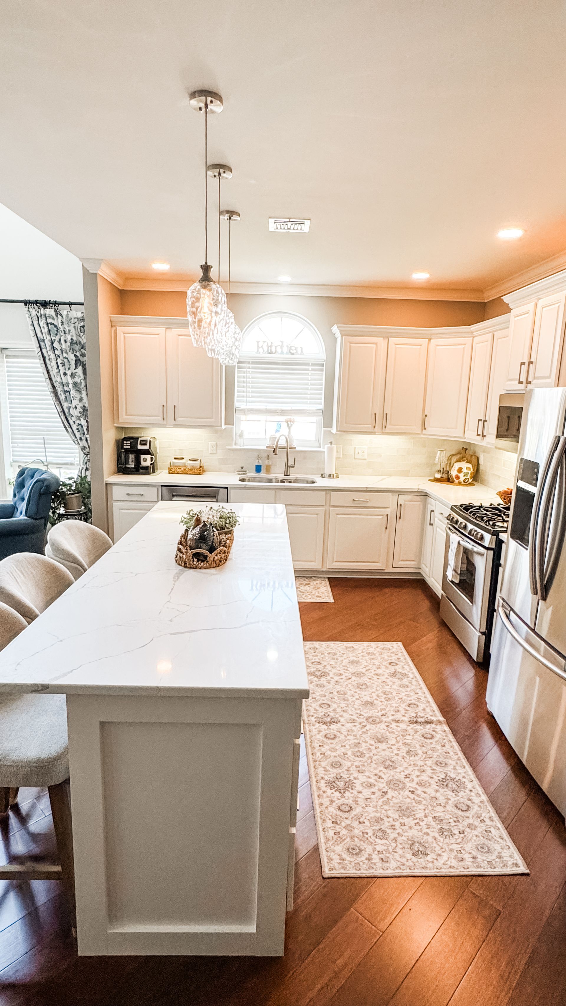 White kitchen with long island, cabinets, and stainless steel appliances, hardwood floors.