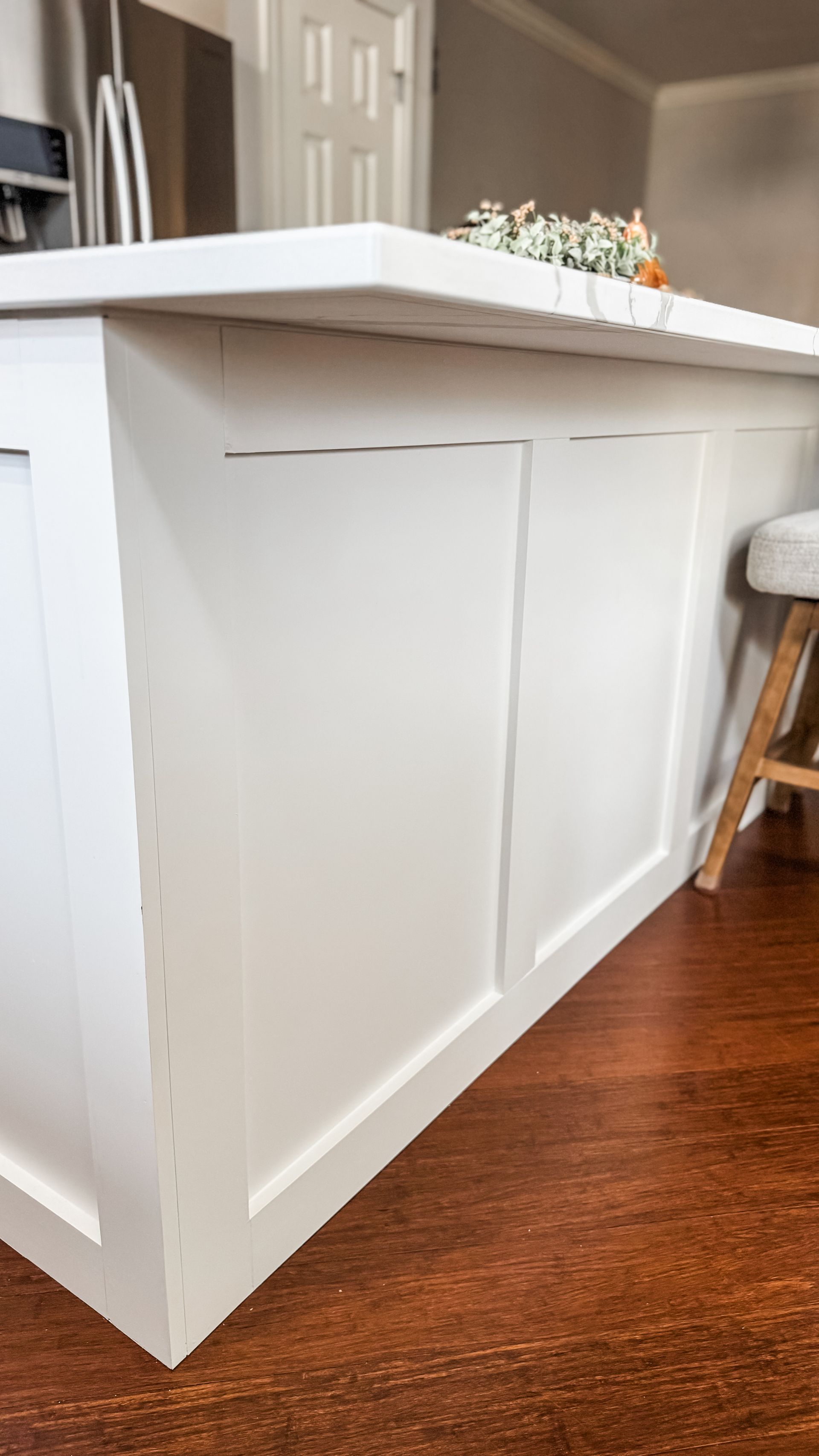 White kitchen island with paneling against dark wood floor.