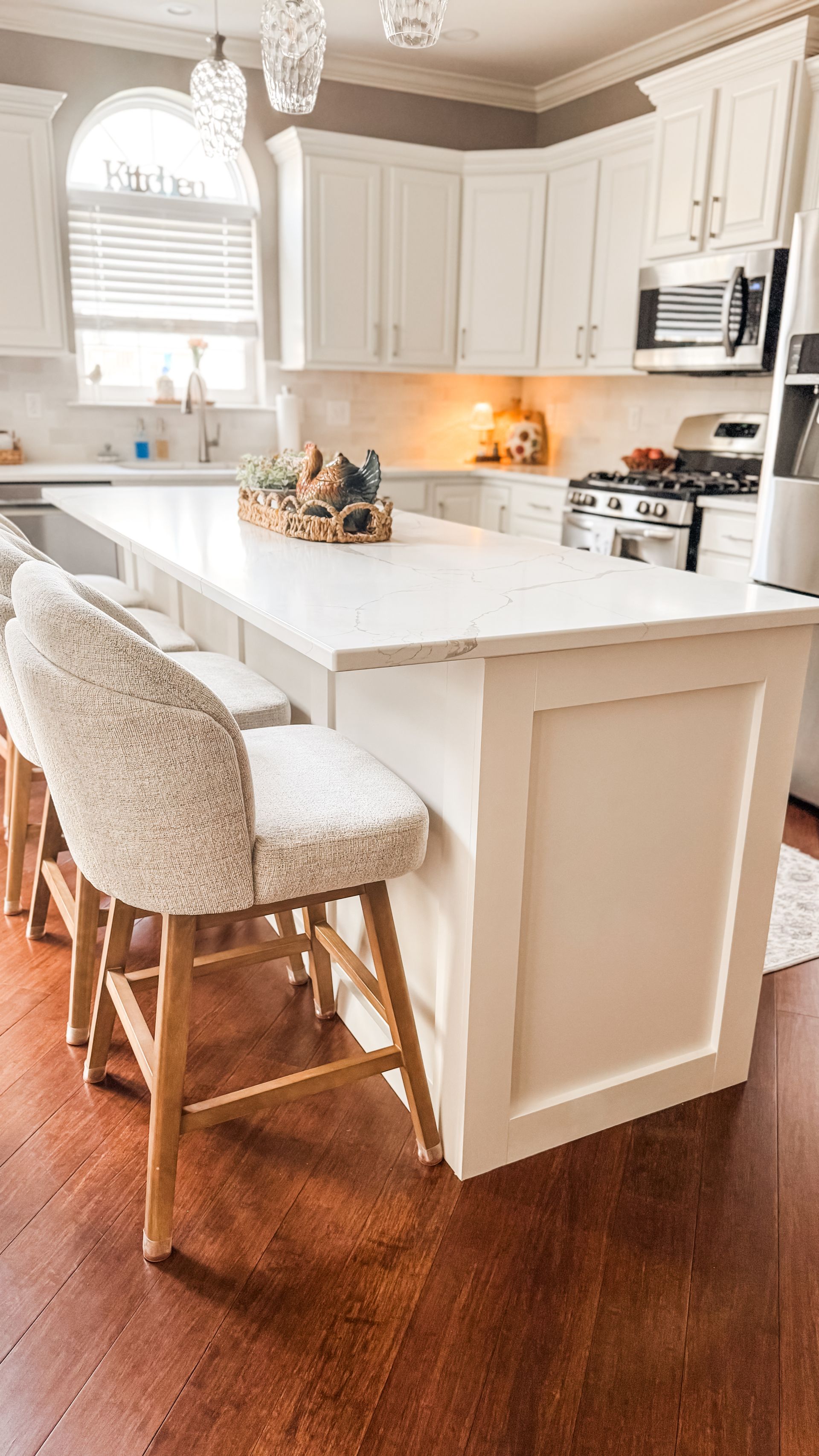 Kitchen with white cabinets, island, and bar stools, brown floor.
